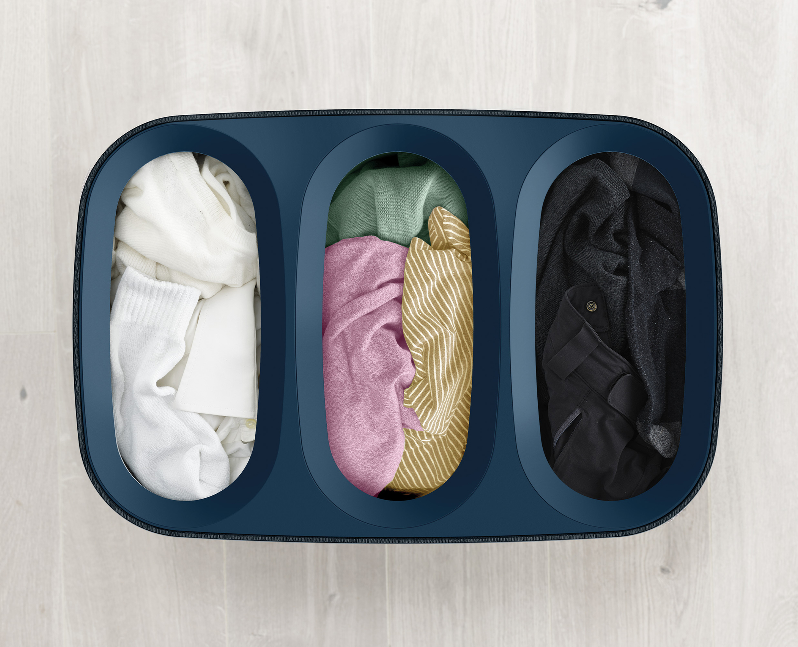 Un clasificador de ropa azul oscuro con tres compartimentos llenos de ropa blanca, rosa/amarilla y negra, sobre suelo de madera clara.
