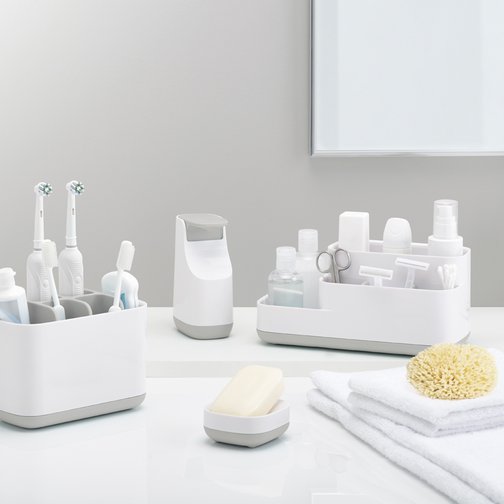 Encimera de baño con artículos de aseo. Incluye cepillos de dientes, jabón, toallas y una esponja. La combinación de colores es blanco y gris.