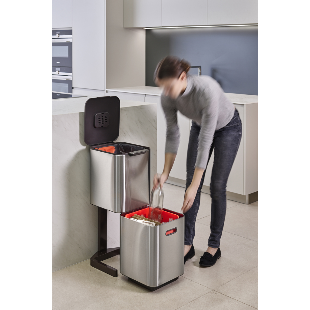 Una mujer pone una botella de vidrio en un contenedor de reciclaje. El contenedor está en una cocina, con un diseño moderno.