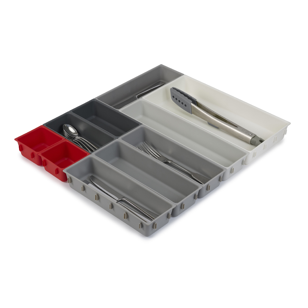 Un organizador de cajones de cocina dividido. Contiene cucharas, tenedores, cuchillos y pinzas. Compartimentos rojos, grises y blancos visibles.
