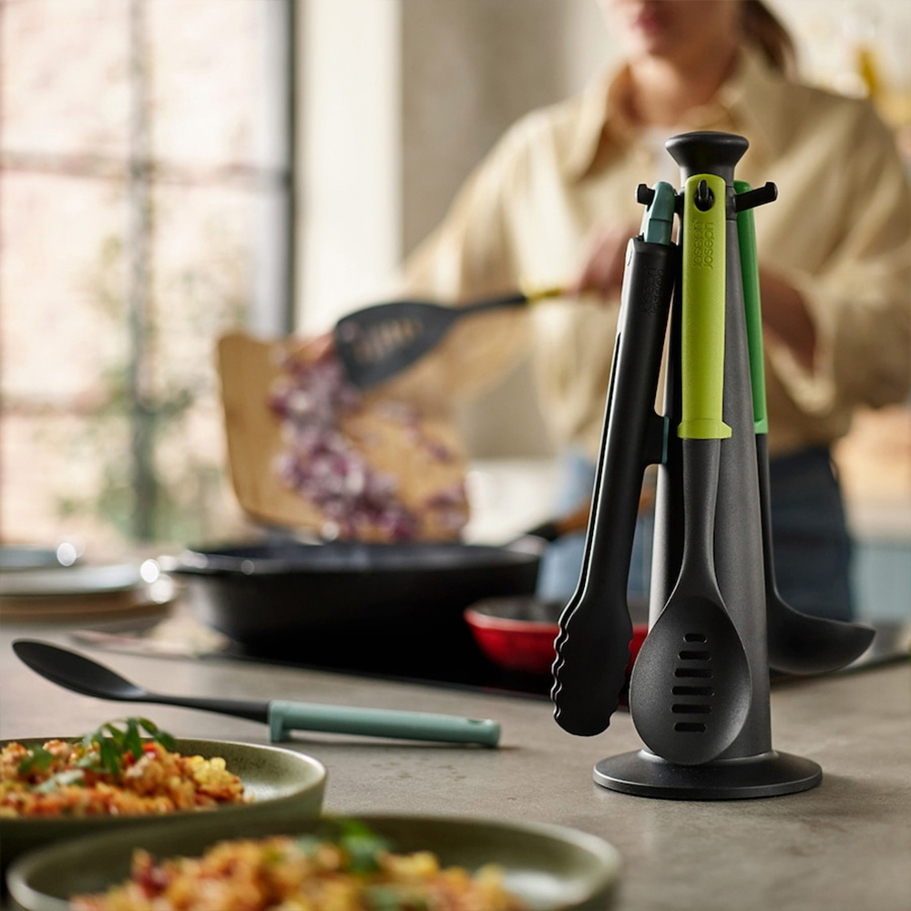 Utensilios de cocina en un soporte. Una persona cocina en el fondo. Platos con comida están en primer plano.