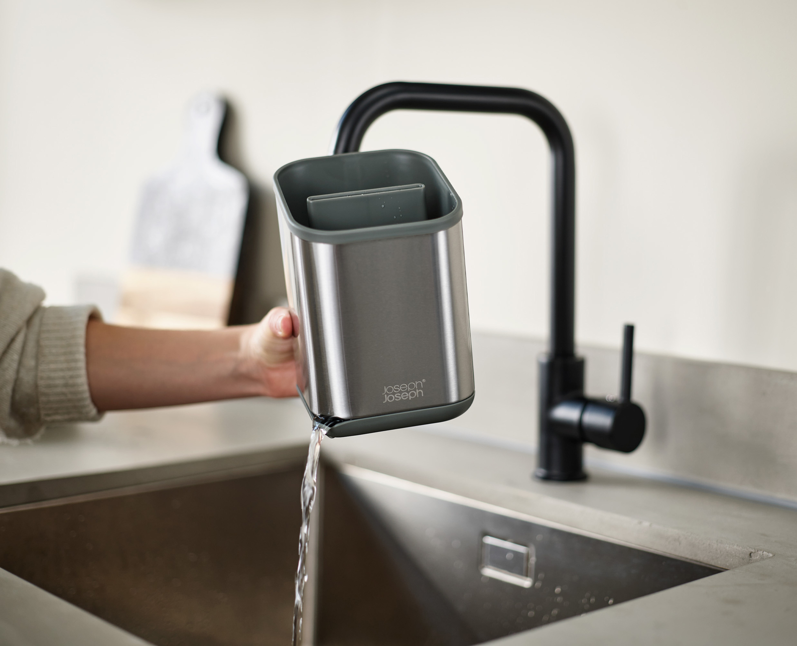 Una persona sta versando acqua da un utensile in acciaio in un lavandino. Si vede un rubinetto nero.