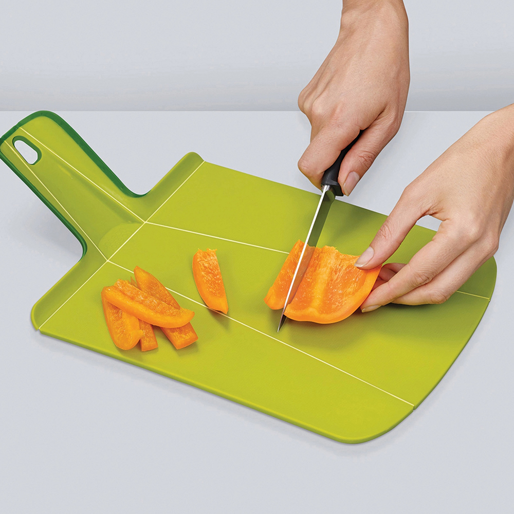Una persona está cortando un pimiento naranja en una tabla de cortar verde con un cuchillo negro. Hay trozos de pimiento cortados en la tabla.