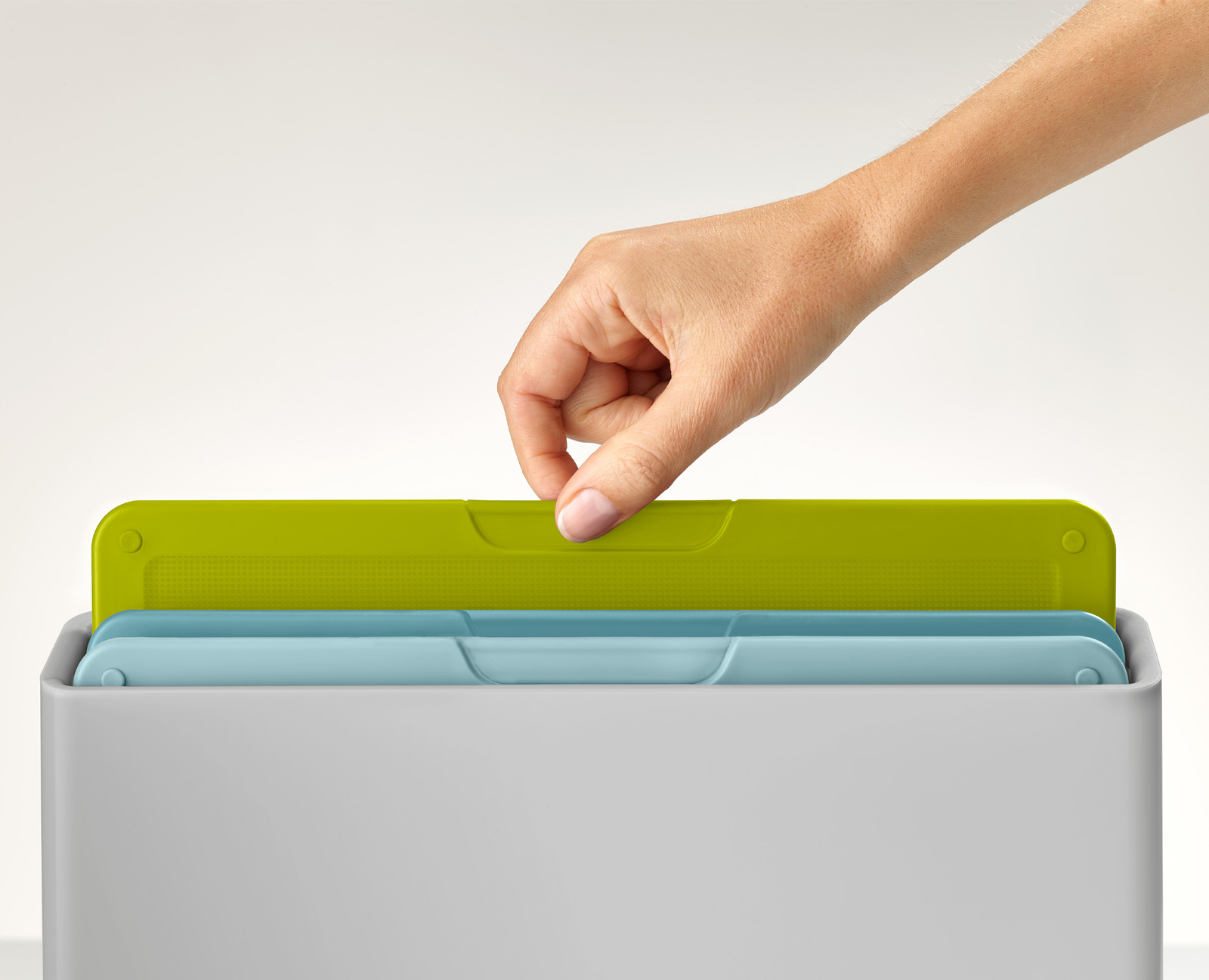 Una mano saca una tabla de cortar verde de un recipiente gris. Debajo hay una tabla azul.