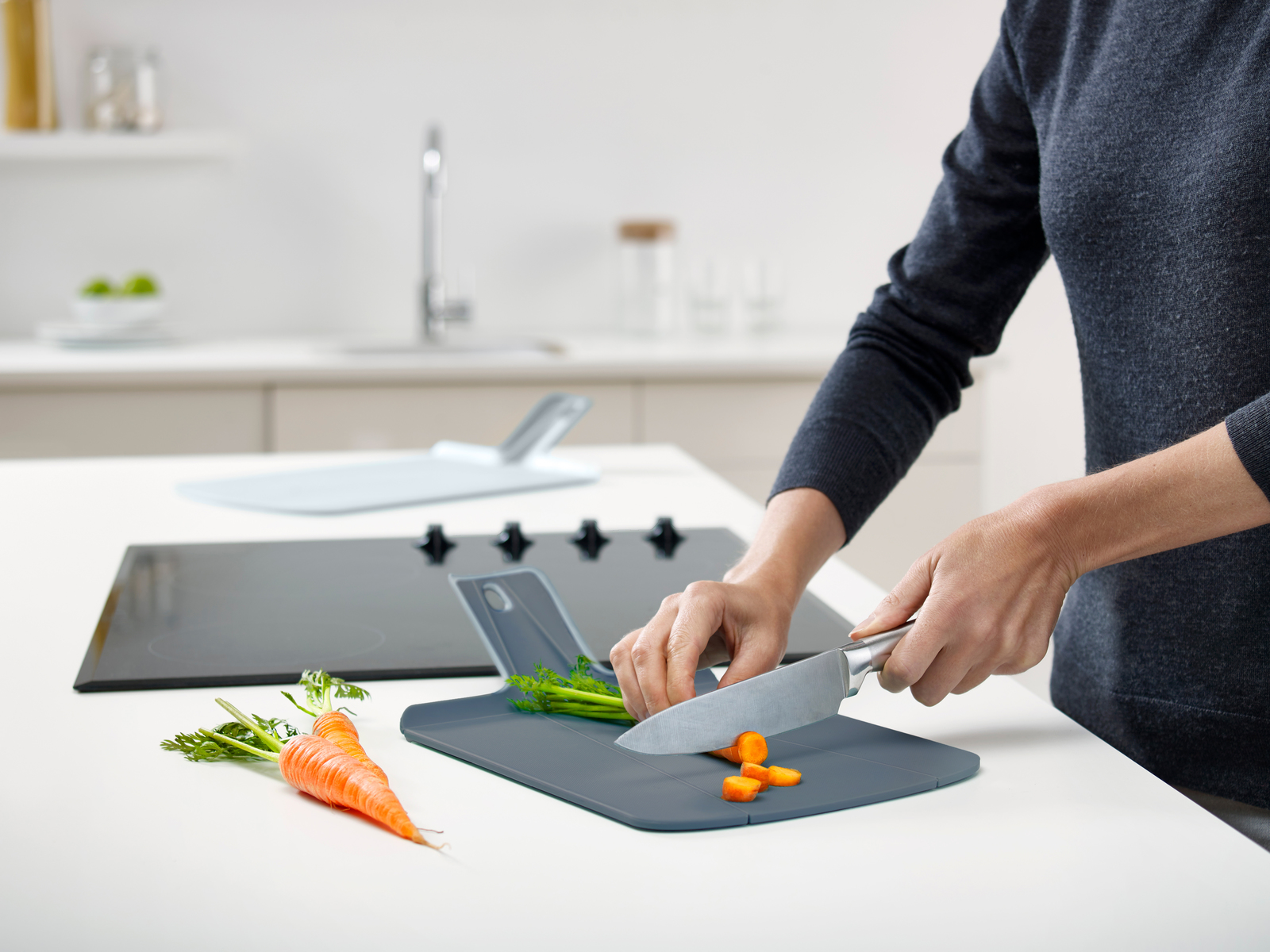 Una persona está cortando una zanahoria en una tabla de cortar gris con un cuchillo. Hay otras zanahorias cerca. Ambiente de cocina.