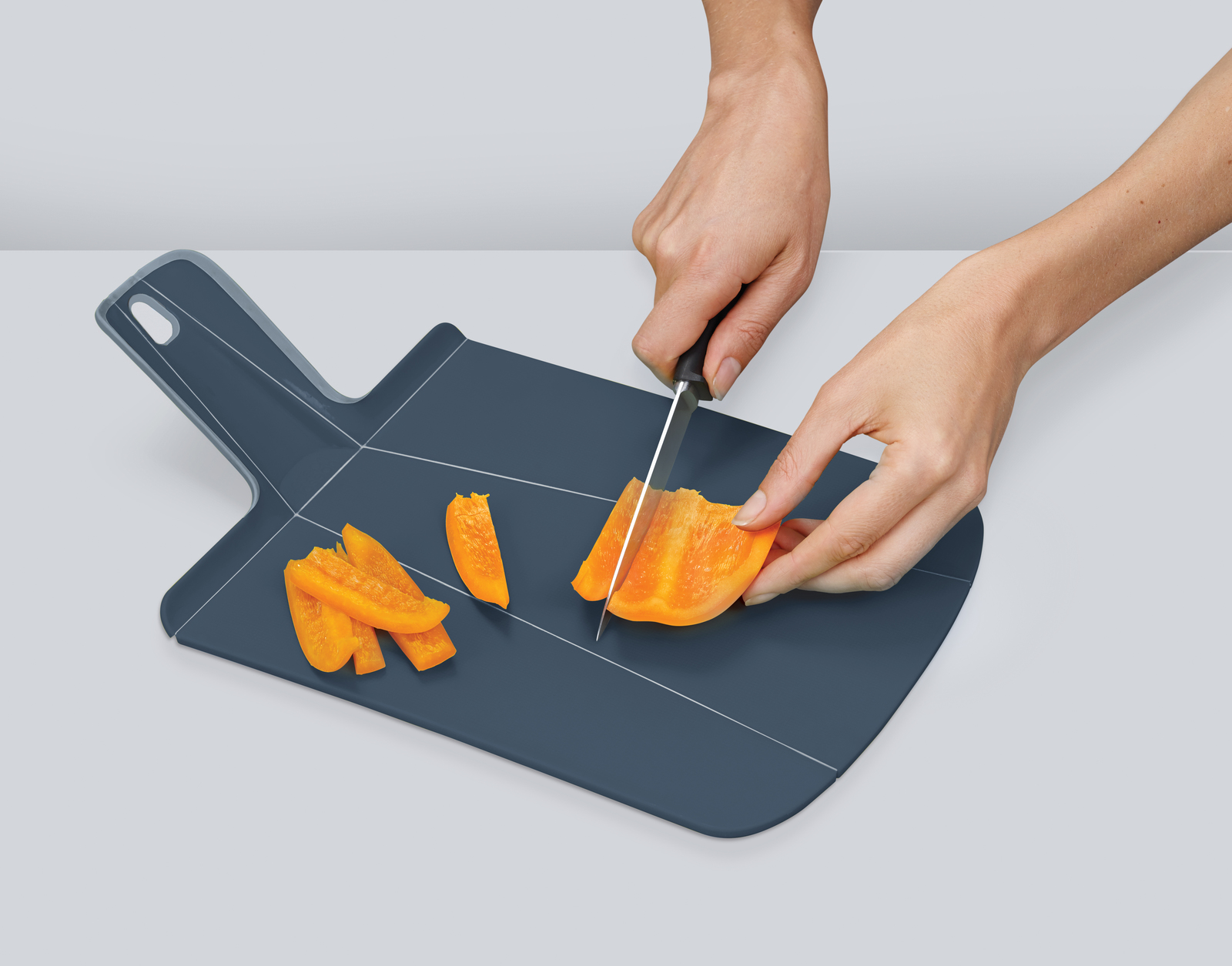Manos cortando pimiento amarillo en una tabla de cortar azul oscuro. Trozos de pimiento cortados ya están en la tabla.