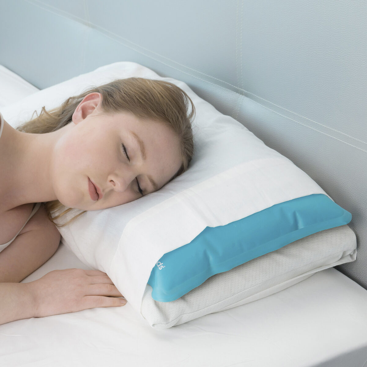 Una donna dorme su un cuscino con un impacco di gel blu sopra. È su un letto bianco, con una testata azzurra.