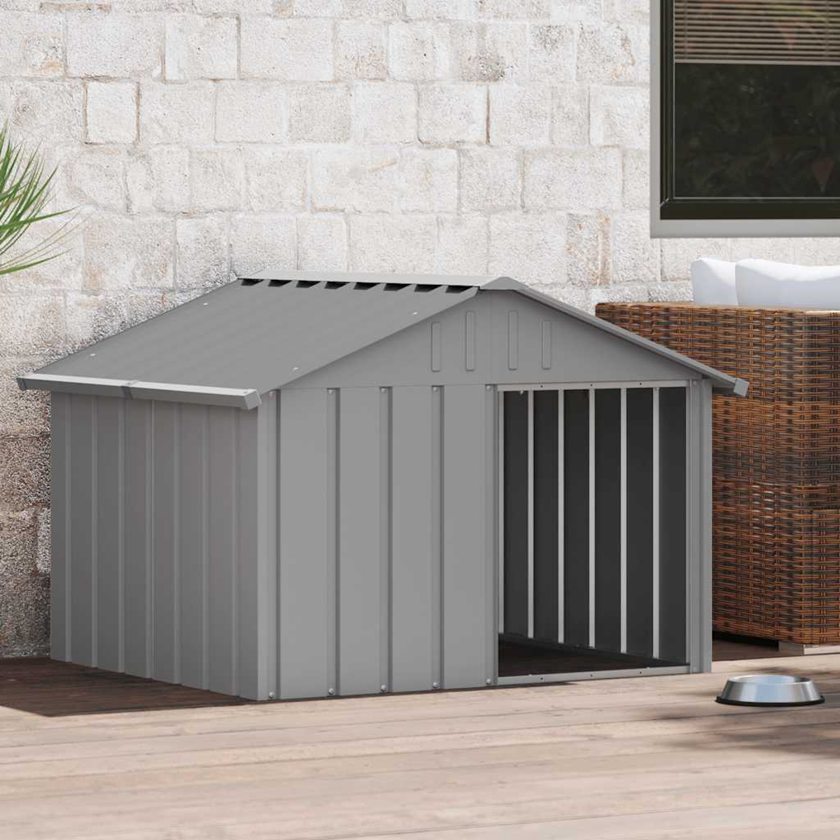 Graues Hundehütte auf Holzterrasse. Das Haus hat ein schräges Dach und einen vergitterten Eingang. Eine Wasserschüssel steht daneben.