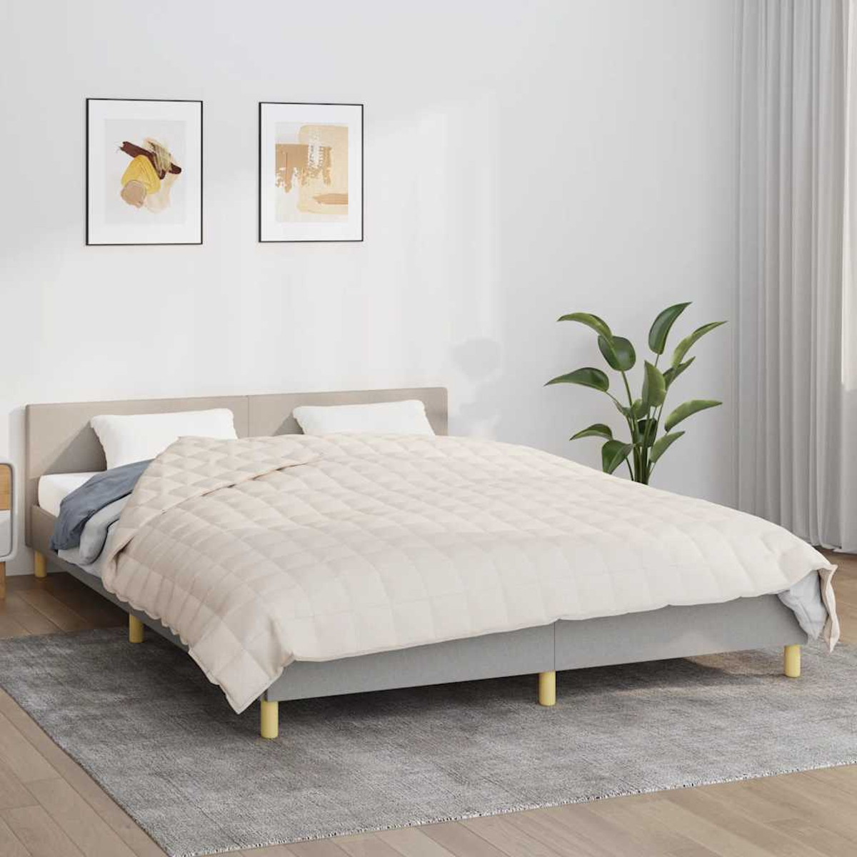 Ein Bett mit cremefarbenem Steppbett, zwei gerahmten Bildern, einer Pflanze und einem grauen Teppich. Das Bett hat einen grauen Rahmen und eine beige Kopfstütze.