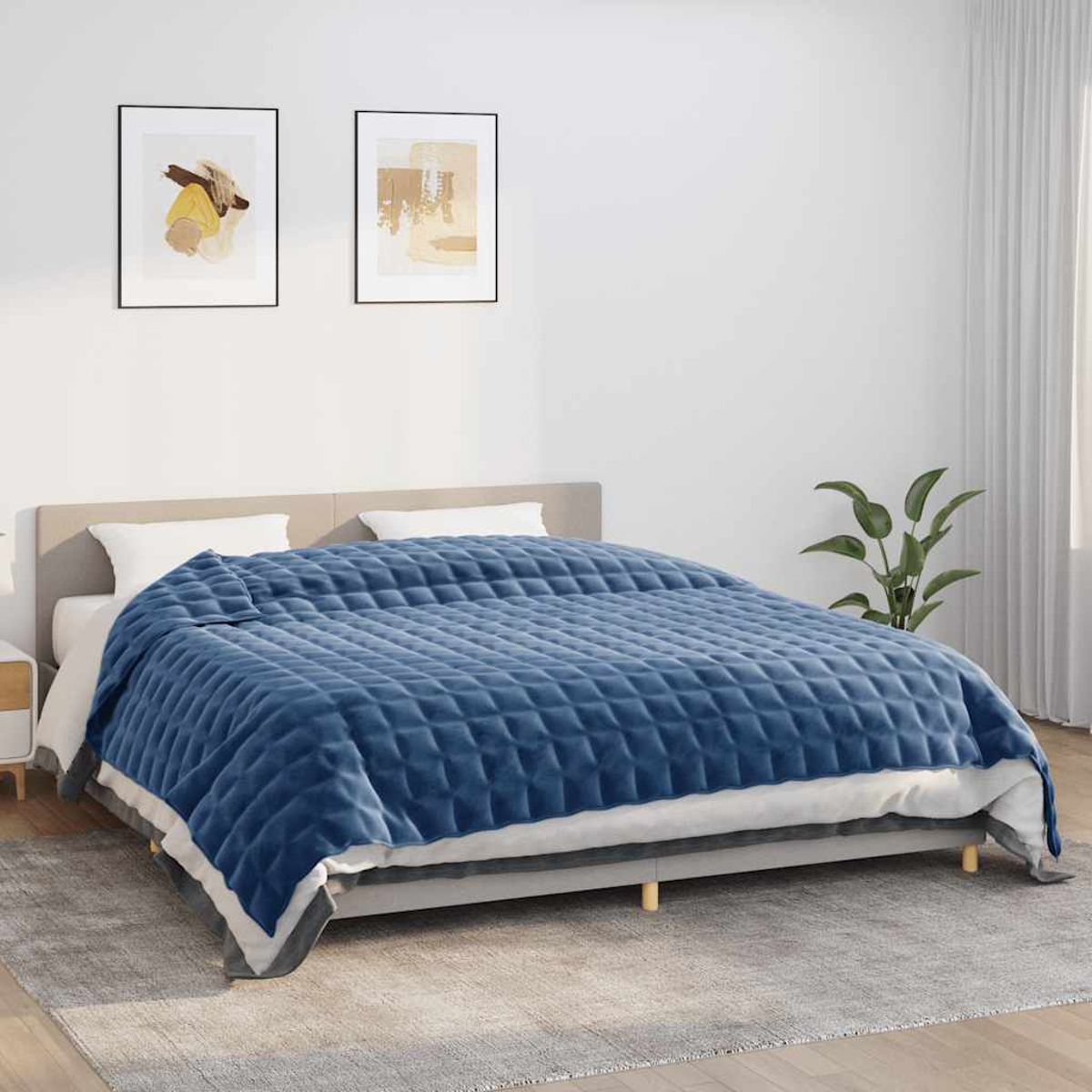 Ein Bett mit einer blau gesteppten Decke. Zwei gerahmte Kunstwerke hängen darüber. Eine kleine Pflanze steht neben einem weißen Vorhang.