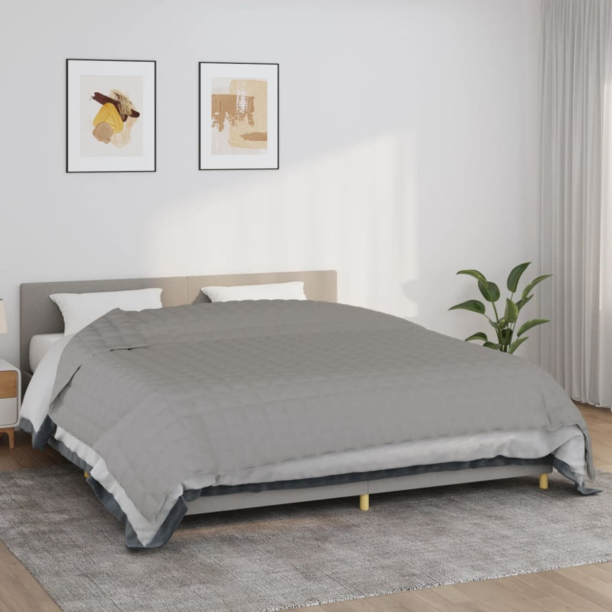 Ein Bett mit grauer Decke, zwei gerahmten Bildern, einer Pflanze und einem grauen Teppich. Weiße Wände und Vorhänge.