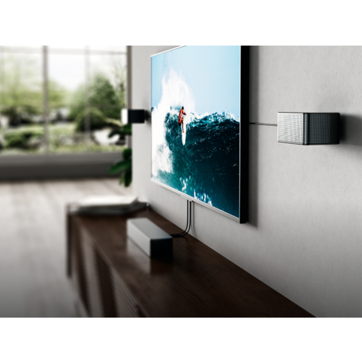 Telewizor na ścianie z surferem na ekranie. Głośniki na ścianie. Soundbar znajduje się na drewnianej szafce pod telewizorem.