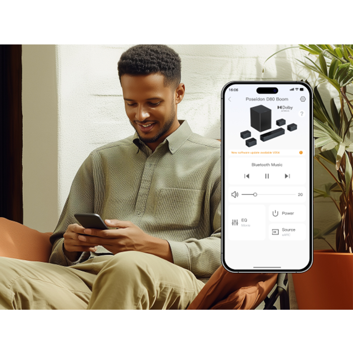 Mężczyzna uśmiecha się, trzymając telefon z aplikacją głośnikową. Po prawej stronie roślina. Mężczyzna ma na sobie zieloną koszulę i spodnie khaki.