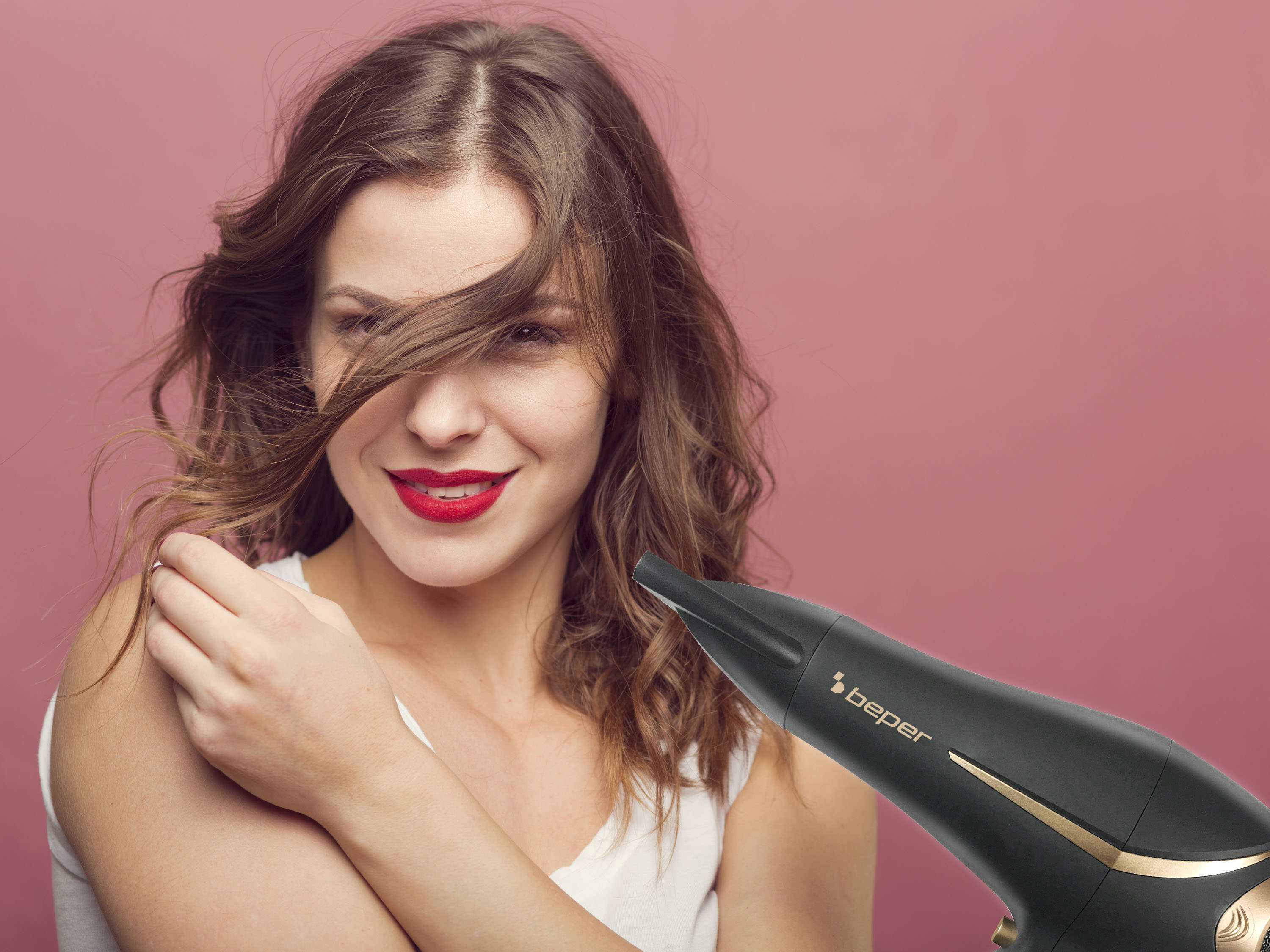 Donna con capelli fluenti sorridente, tiene un asciugacapelli. Sfondo rosa.