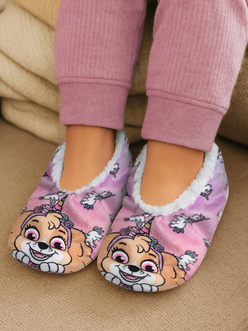 Kinderfüße in rosa Pyjamas und Paw Patrol-Hausschuhen. Die Hausschuhe sind rosa mit Skys Gesicht, umgeben von Einhörnern.