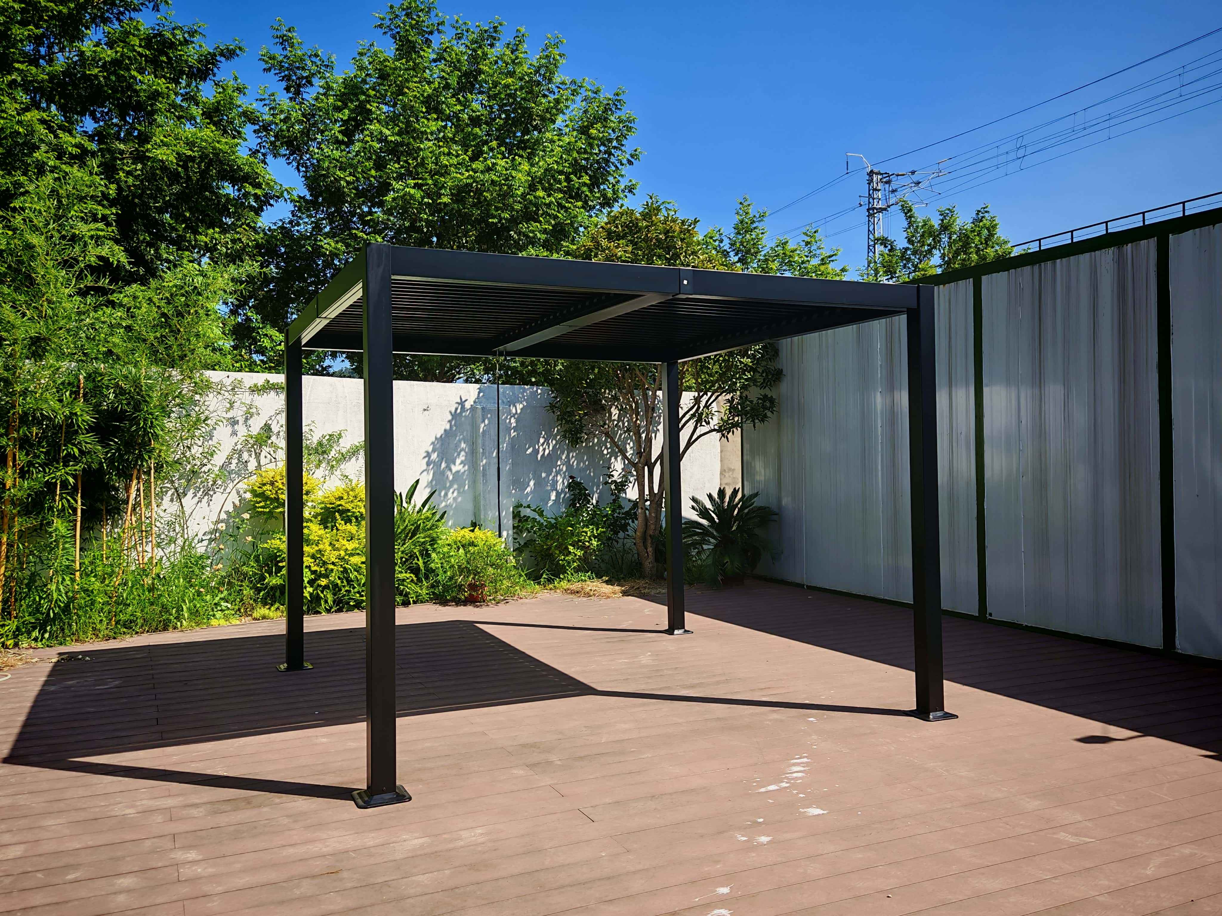Schwarze Pergola auf Holzterrasse. Grüne Pflanzen und Bäume umgeben sie unter blauem Himmel.