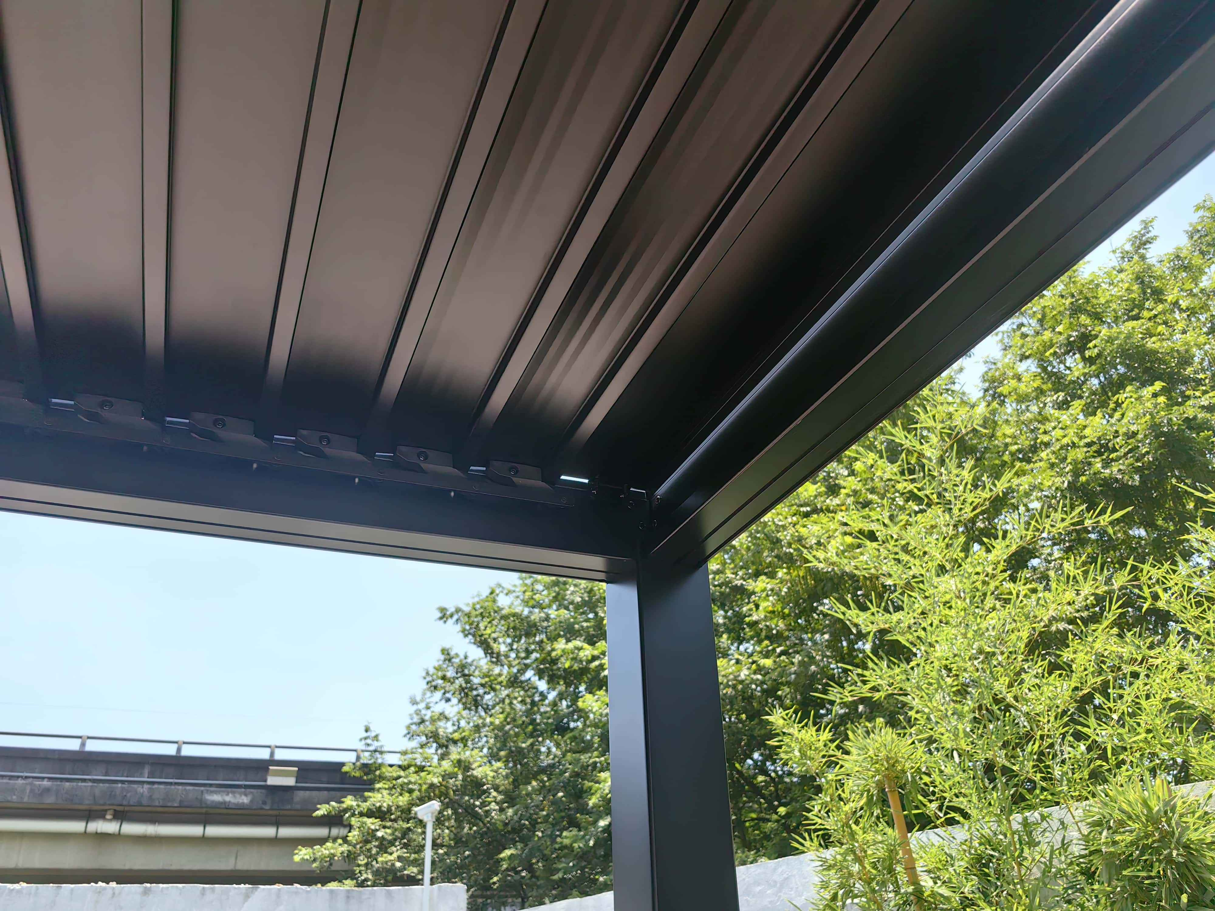 Schwarzes Pergola-Dach mit Stützbalken. Bäume und blauer Himmel im Hintergrund.