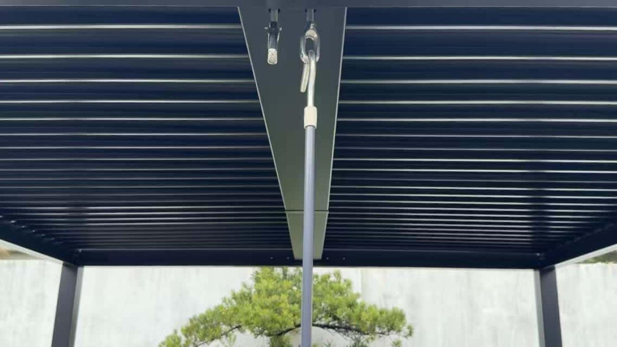 Eine moderne Pergola mit schwarzen Lamellen und Metallstütze. Im Hintergrund ist ein Baum zu sehen.