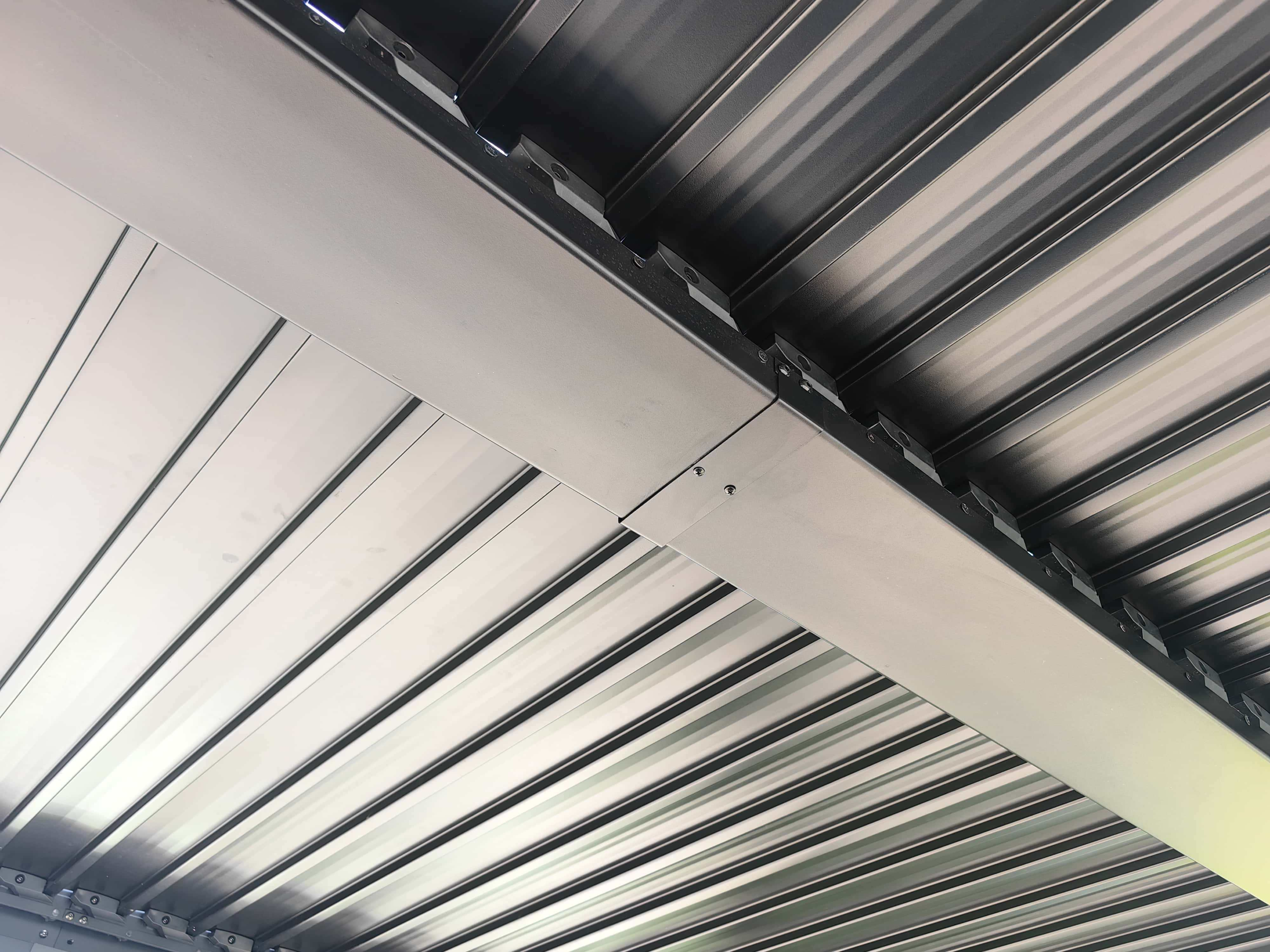 Nahaufnahme einer Metalldecke. Parallele Linien und Balken bilden ein geometrisches Muster. Die Farben sind grau und schwarz.