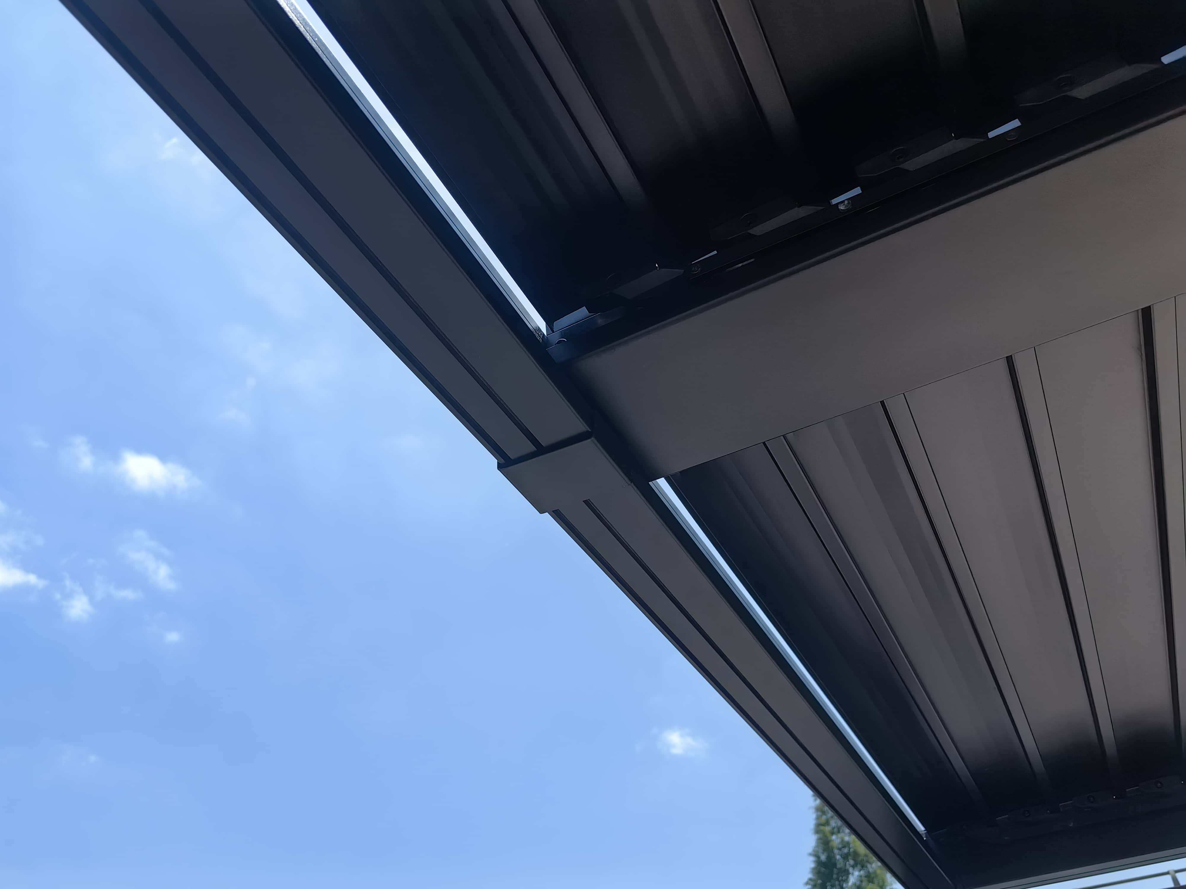 Dunkle, metallische Struktur von unten gesehen vor blauem Himmel. Geometrische Formgebung.