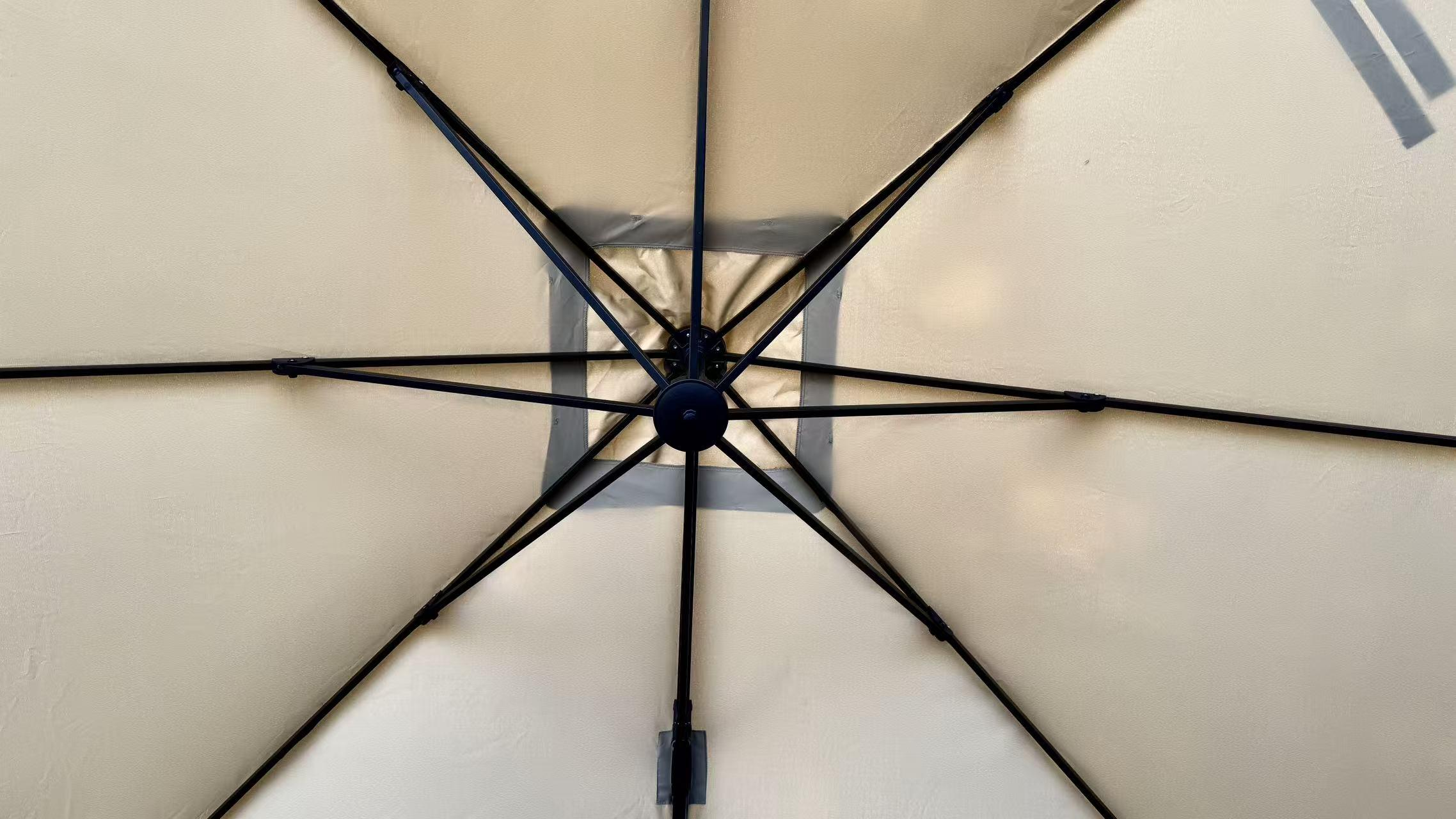 Ansicht von unter einem beigefarbenen Regenschirm. Schwarzer Metallrahmen strahlt von einer zentralen Nabe aus.
