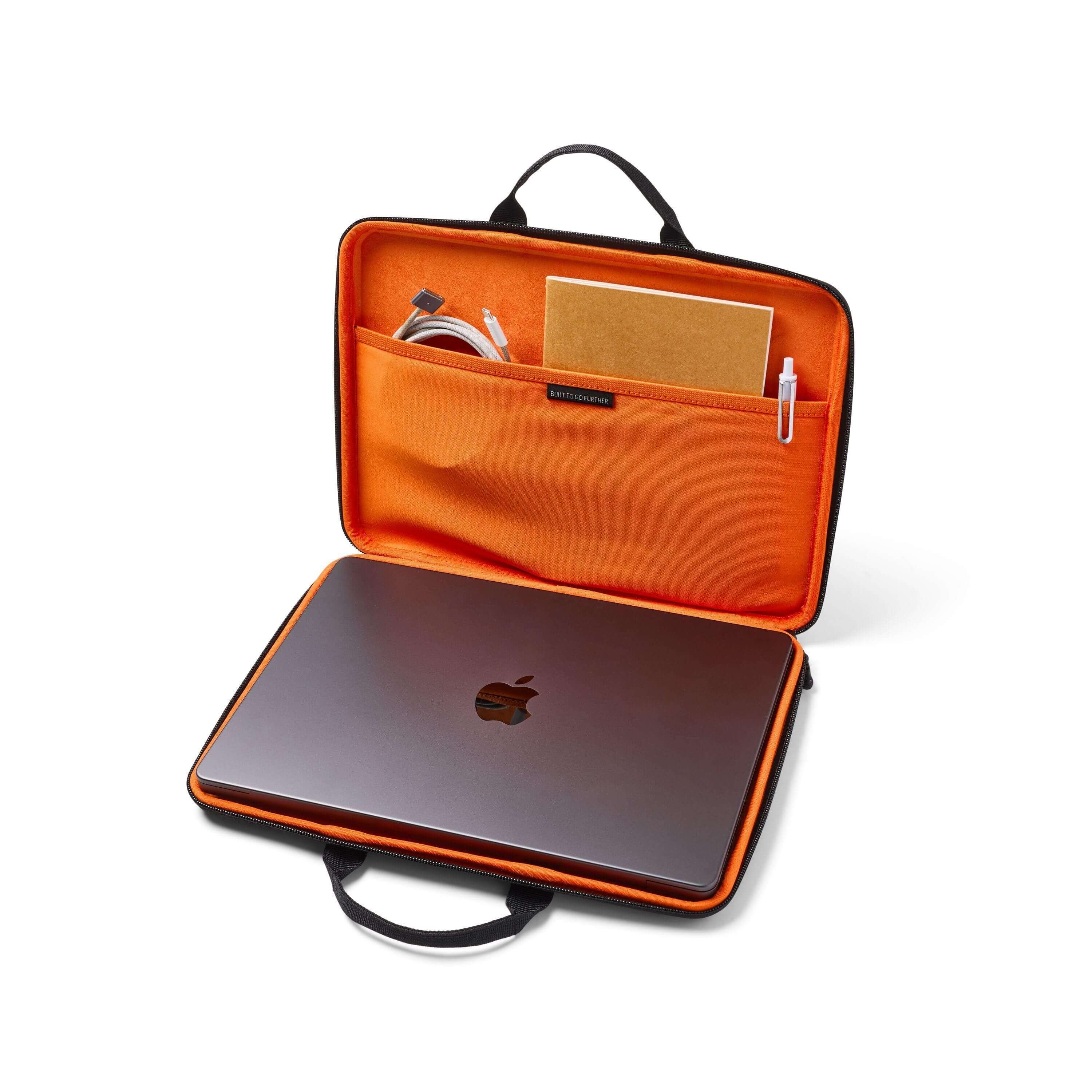 Otwarta torba na laptopa z laptopem w środku. Pomarańczowe wnętrze, czarny uchwyt. Kable i notatnik w kieszeni.