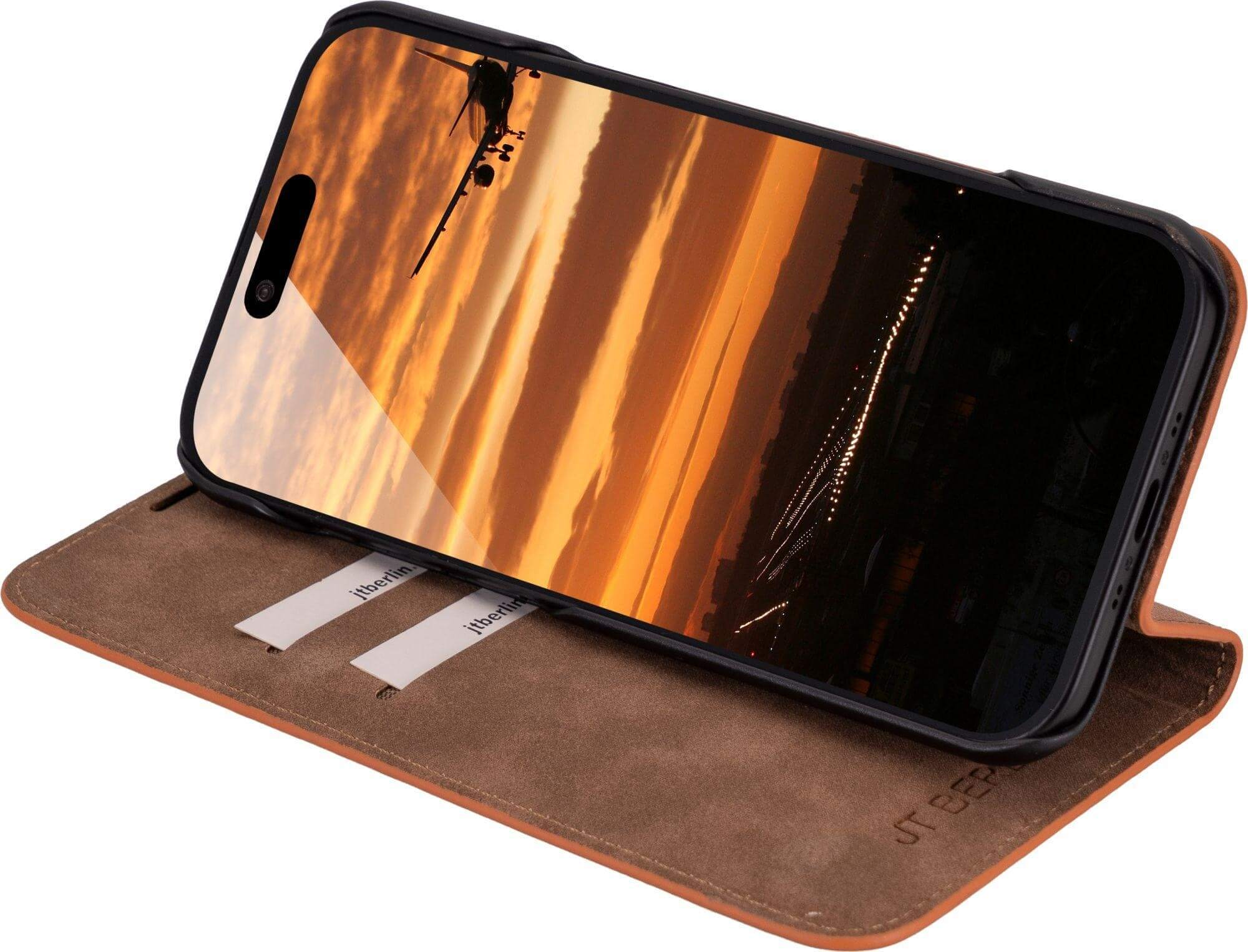Ein Telefon in einer braunen Lederhülle zeigt einen Sonnenuntergang mit der Silhouette eines Flugzeugs. Die Hülle ist offen und zeigt ein braunes Innere.