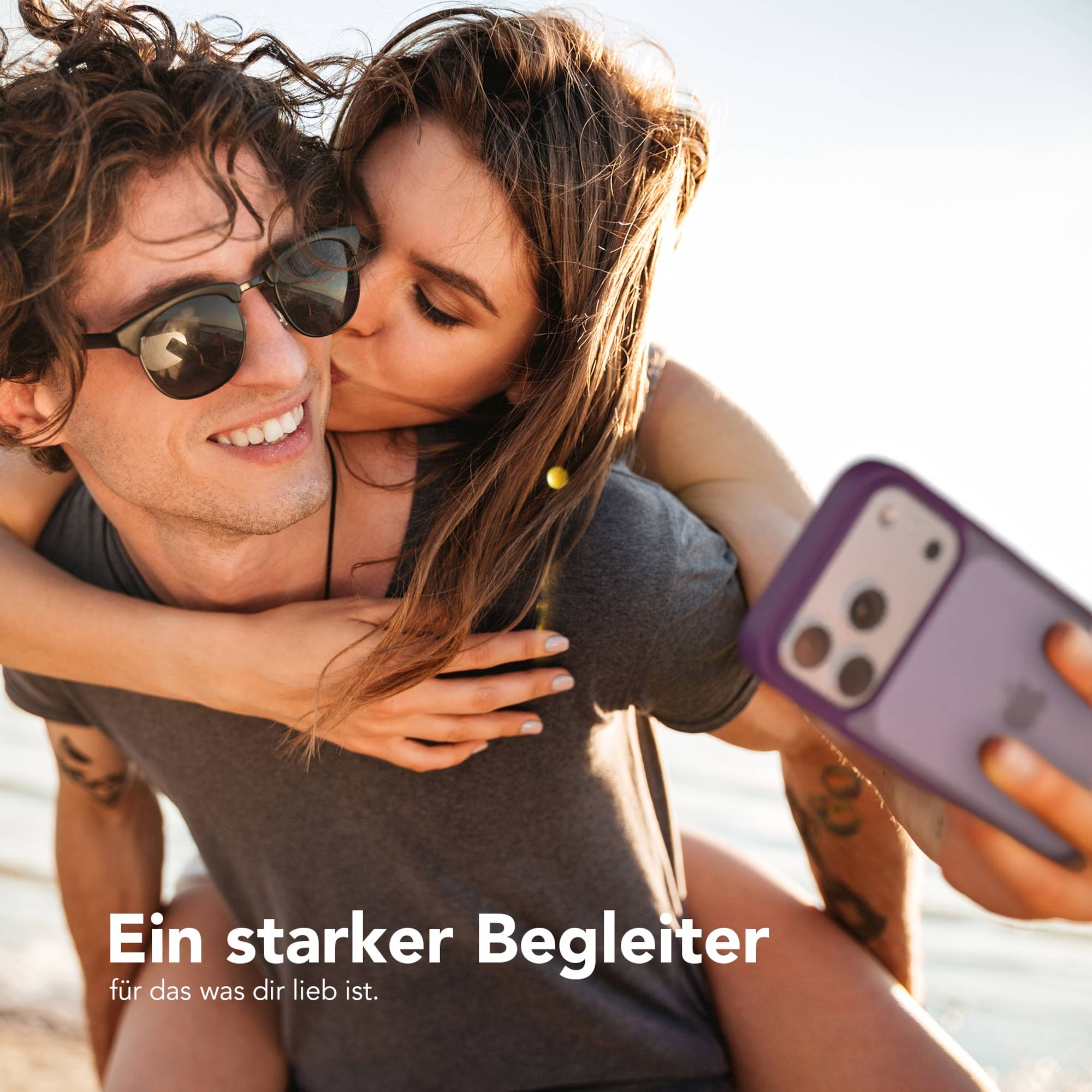 Eine Frau küsst einen Mann auf die Wange. Er trägt eine Sonnenbrille, sie hält ein Telefon. Text: Ein starker Begleiter.