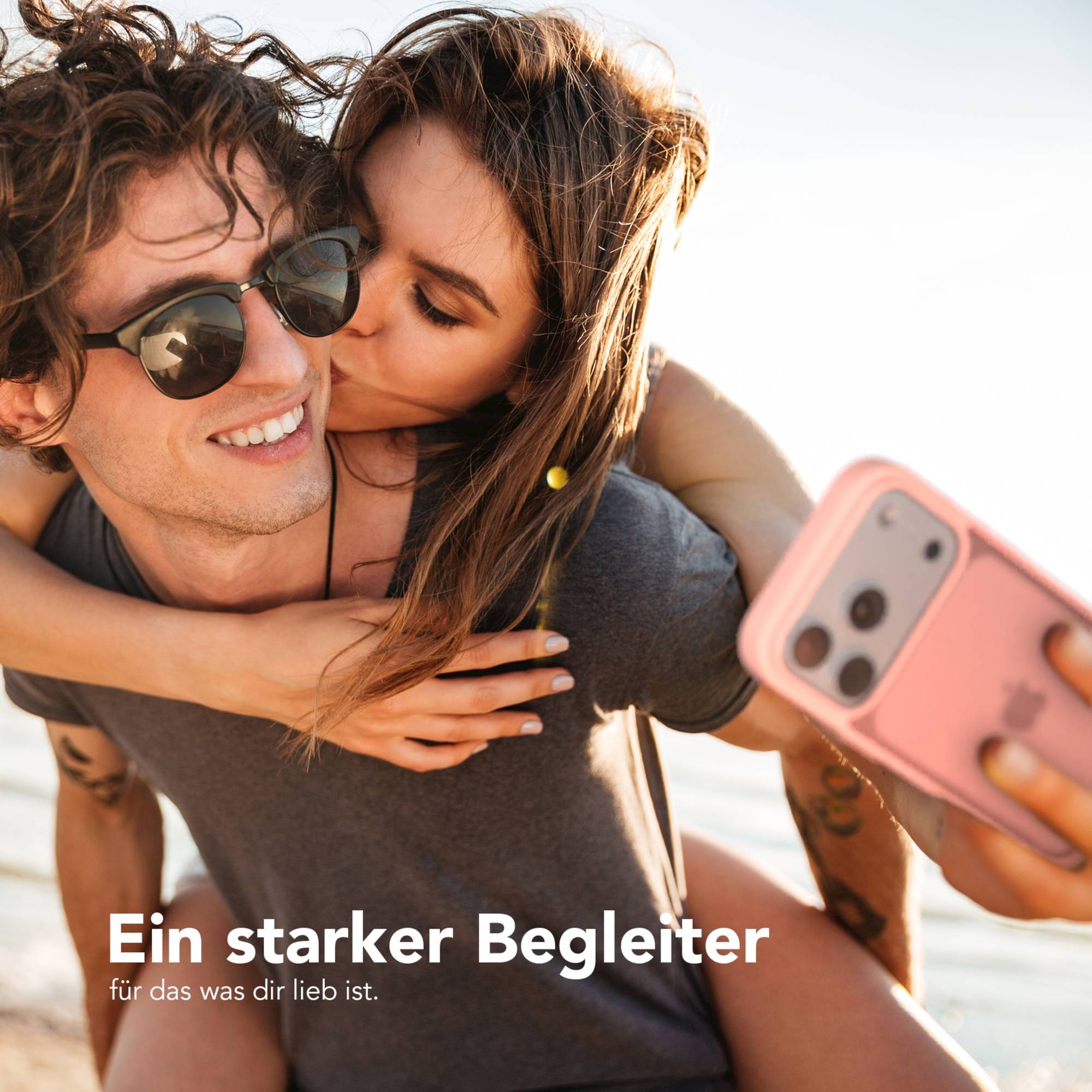Eine Frau küsst einen Mann mit Sonnenbrille. Sie halten ein rosa Telefon. Text: 'Ein starker Begleiter'.