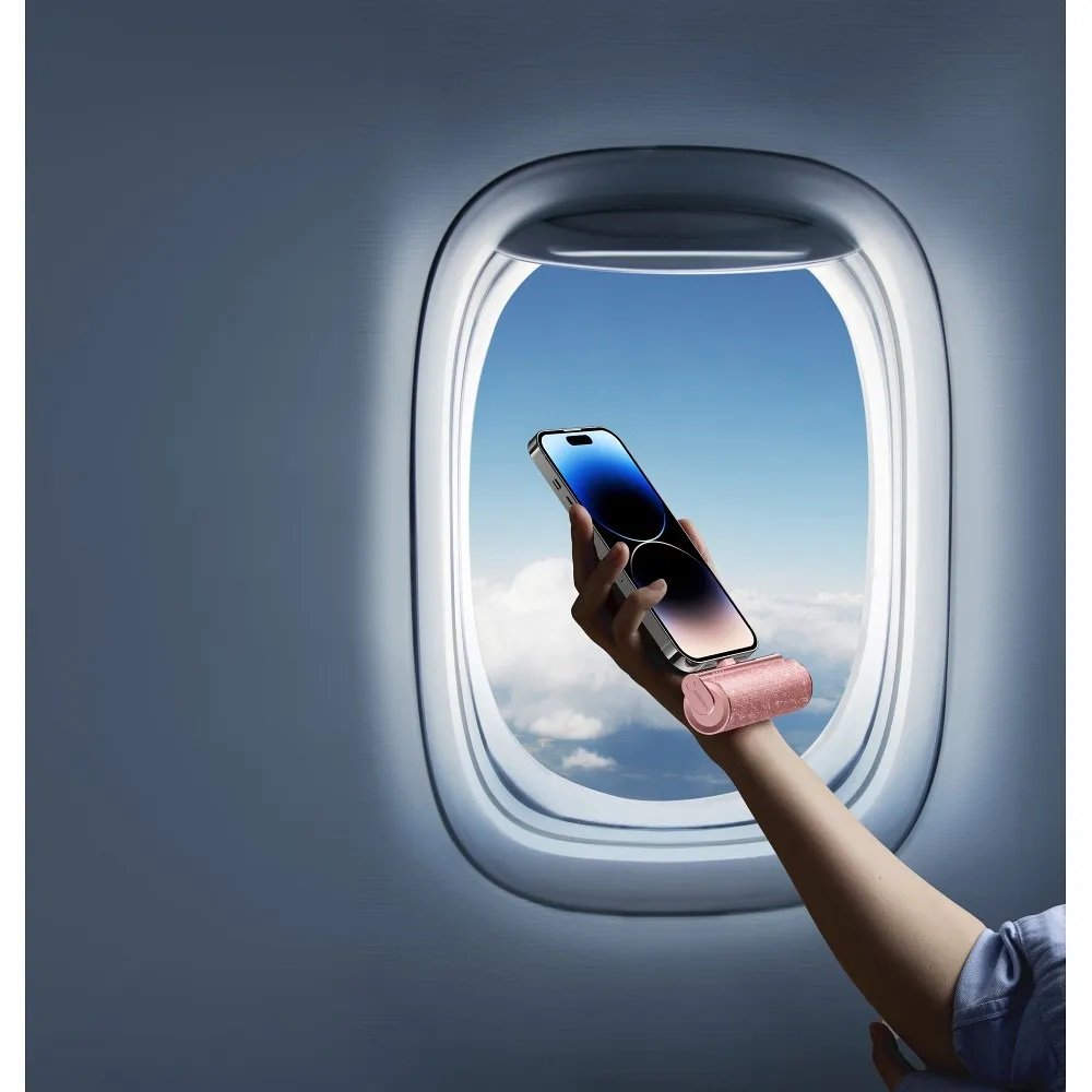 Una mano tiene un telefono davanti a un finestrino di un aereo. La finestra mostra un cielo blu con nuvole. Il telefono è argento.