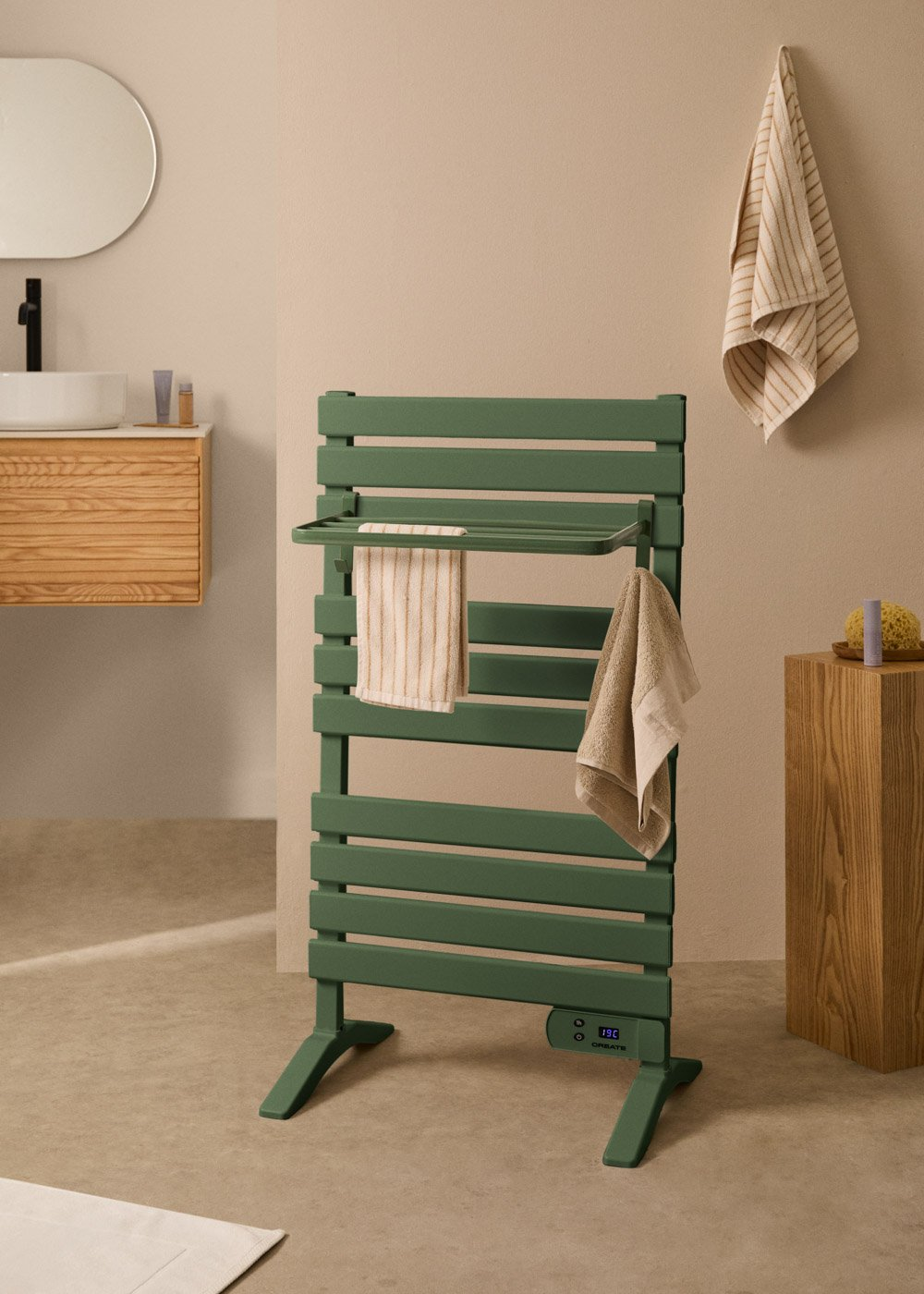 Un calienta toallas verde con toallas colgadas. Pared y suelo beige con mueble y espejo de madera.