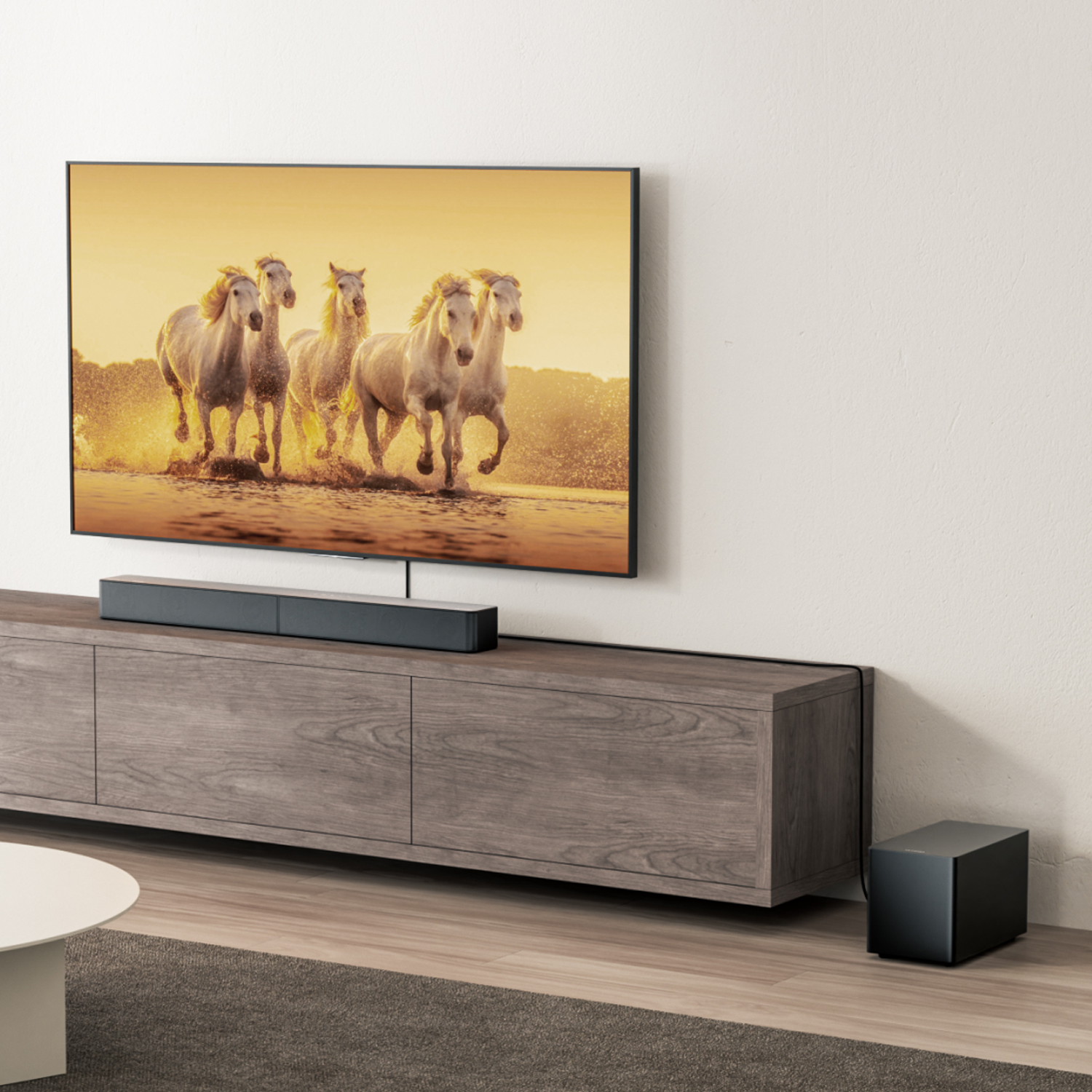 Telewizor pokazuje konie biegnące w wodzie. Pod nim soundbar na drewnianej szafce. Subwoofer na podłodze.