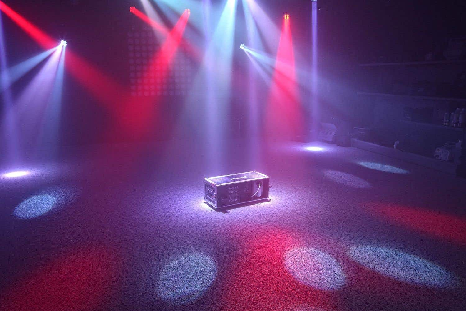 Un escenario con focos rojos y azules brillando sobre una caja. El suelo es oscuro con reflejos.