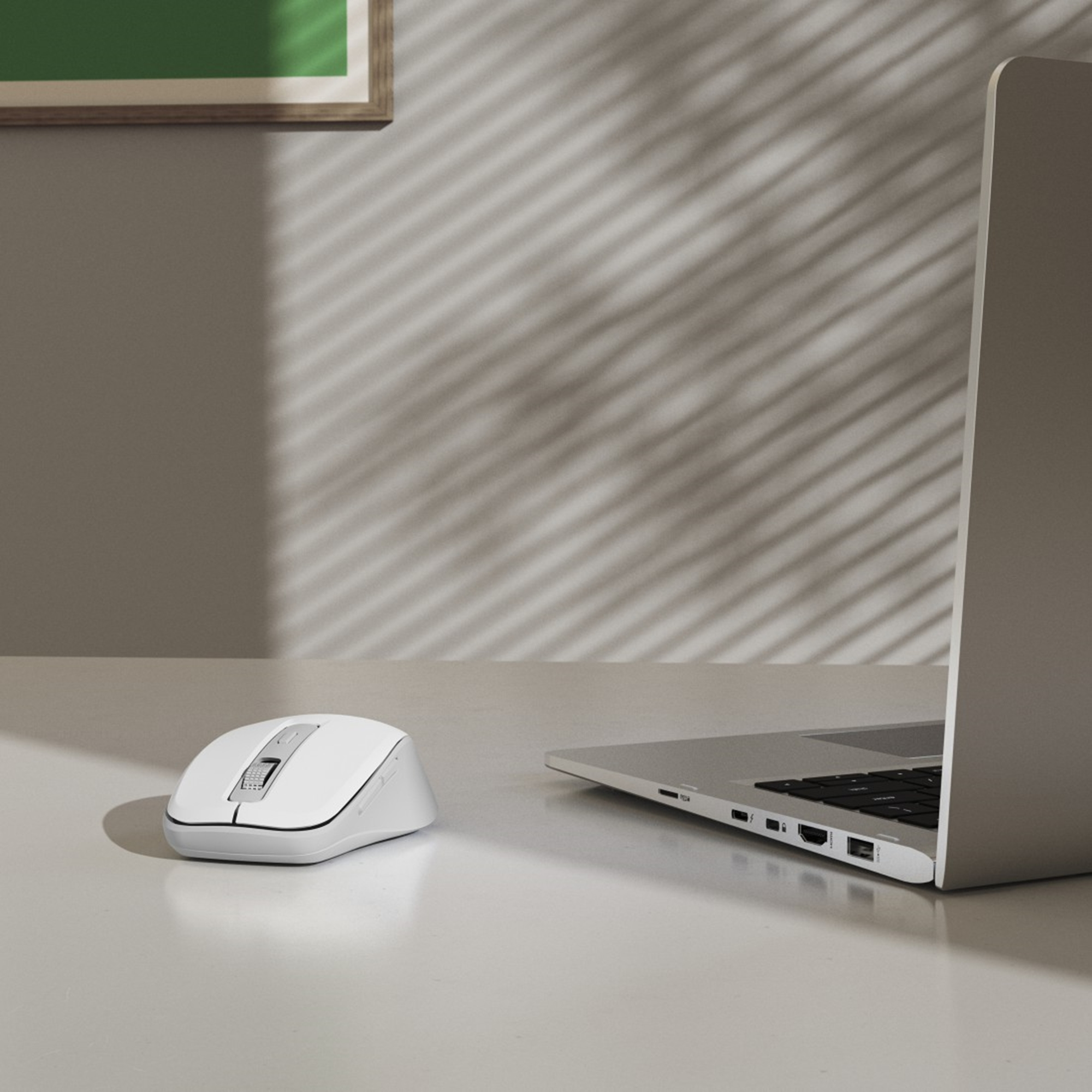 Eine weiße Maus neben einem Laptop auf einem weißen Schreibtisch. Schatten von Jalousien werfen sich auf die dahinterliegende Wand.
