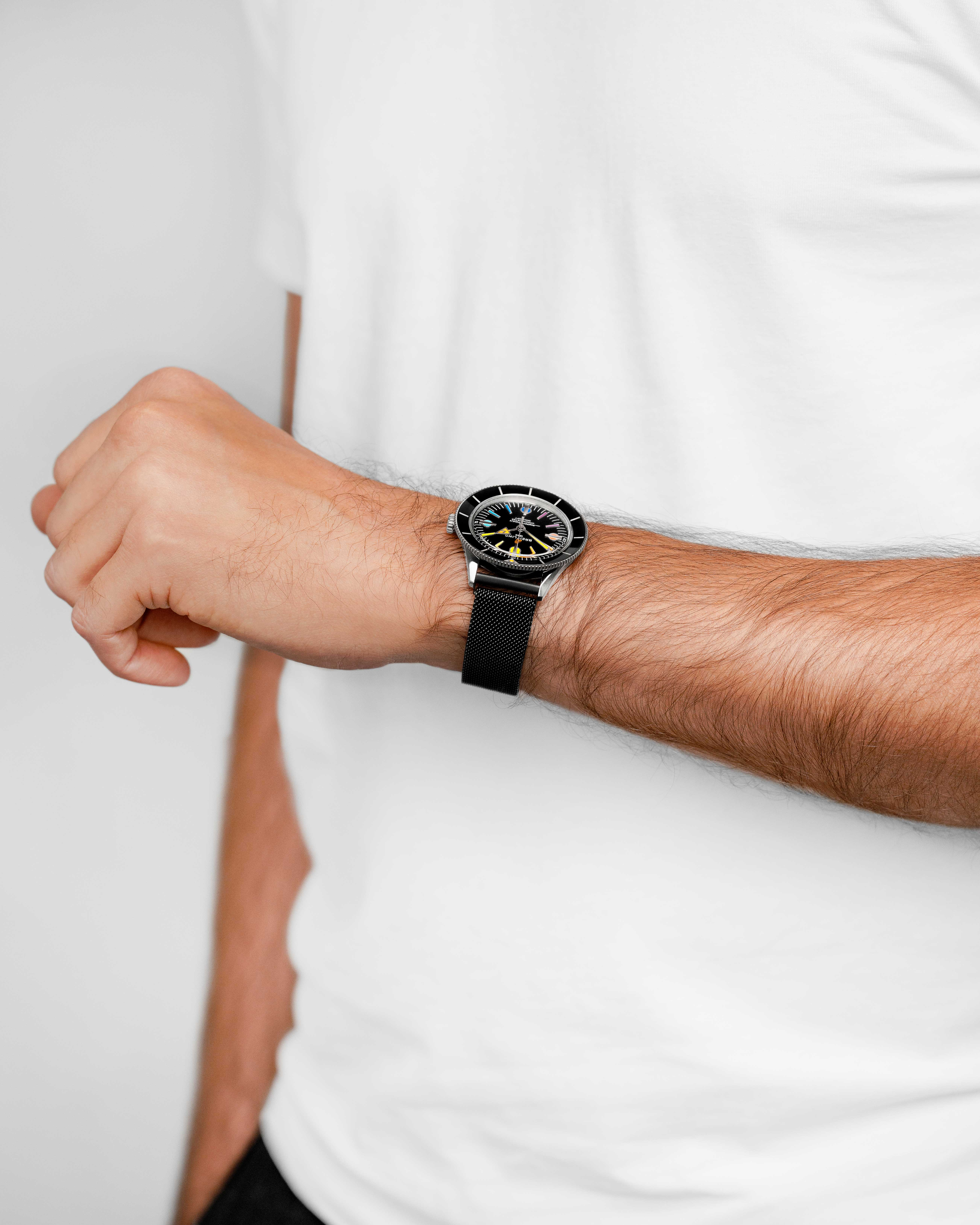 Der Arm einer Person mit einer Uhr am Handgelenk. Die Uhr hat ein schwarzes Band und Ziffernblatt. Die Person trägt ein weißes Hemd.