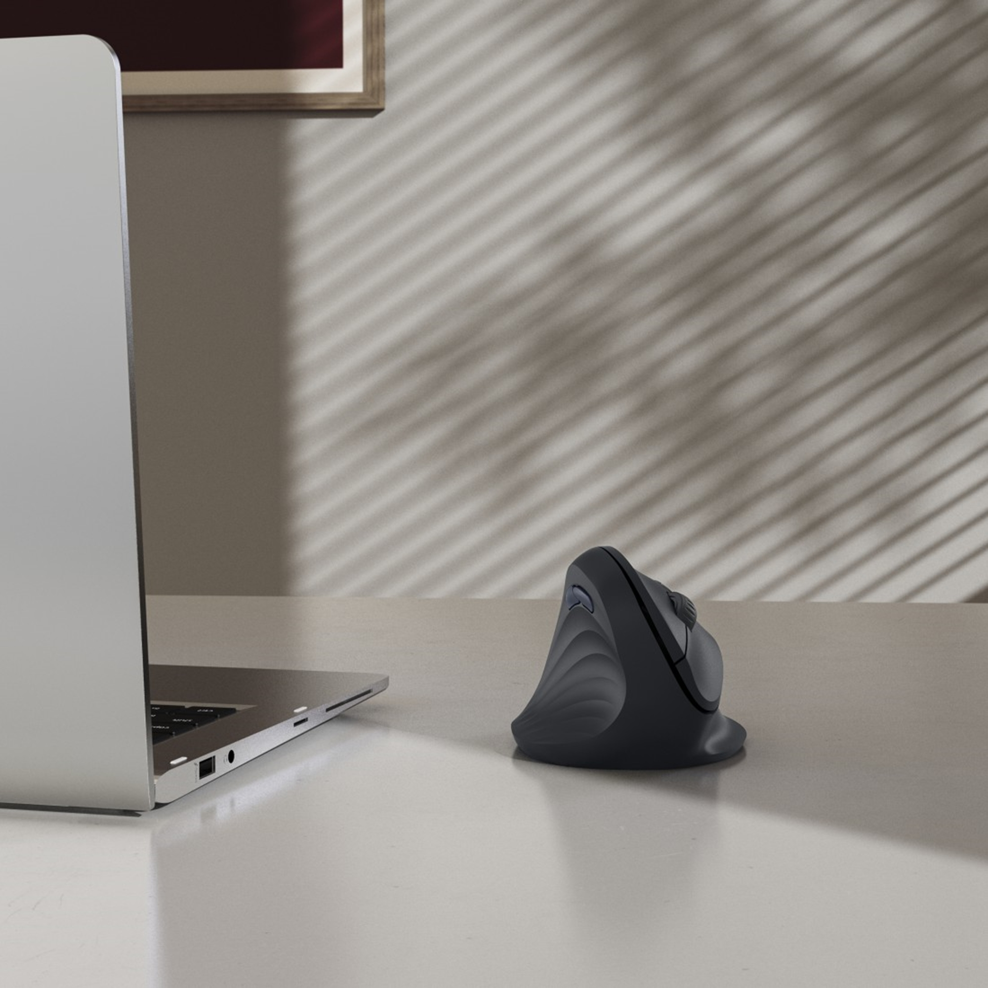 Un mouse ergonomico grigio e un laptop su una scrivania bianca. Ombre di persiane sul muro.