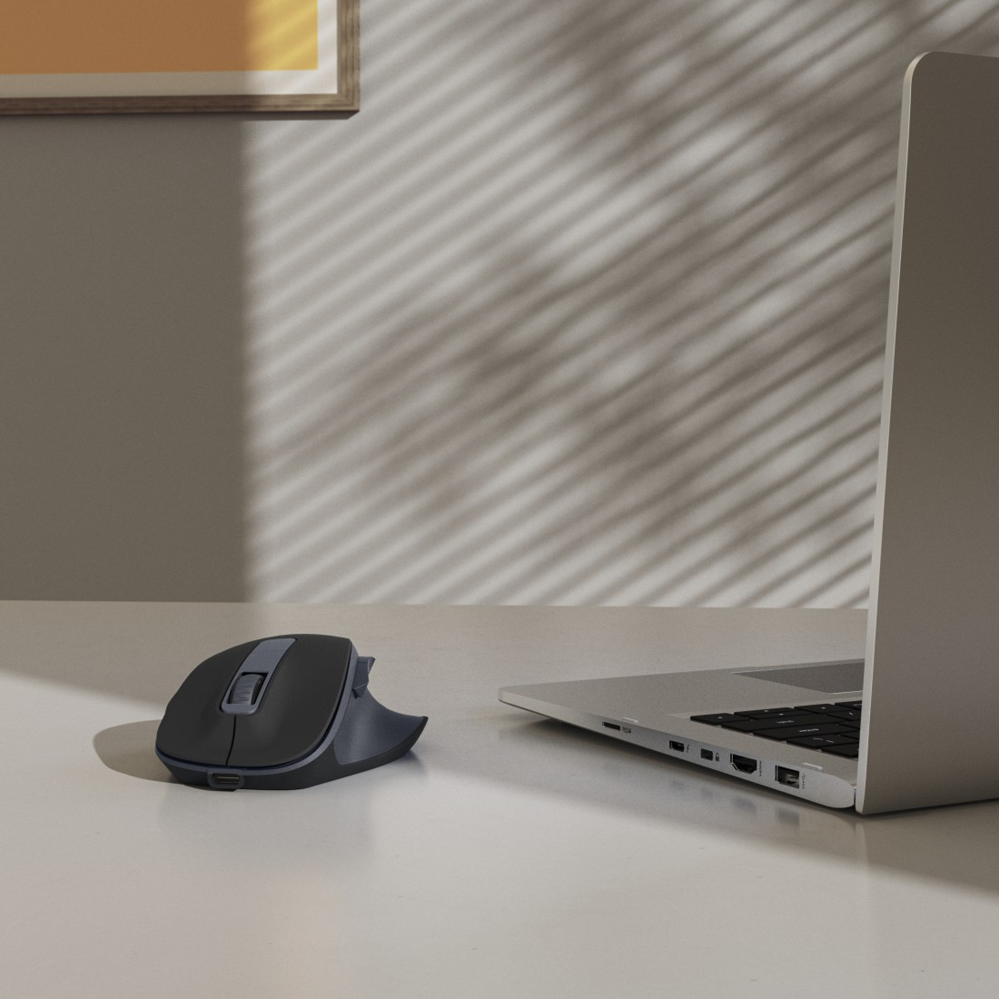 Un mouse per computer nero è accanto a un laptop su una superficie bianca. Le ombre delle persiane sono proiettate sul muro.
