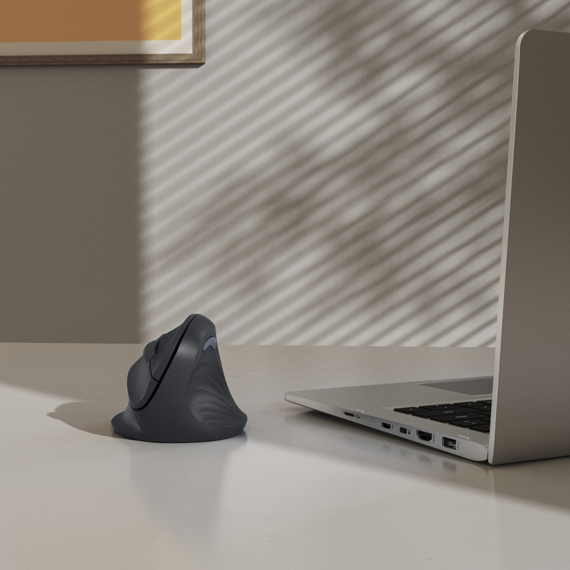 Ergonomiczna szara mysz obok laptopa na białym biurku. Światło i cień na ścianie.