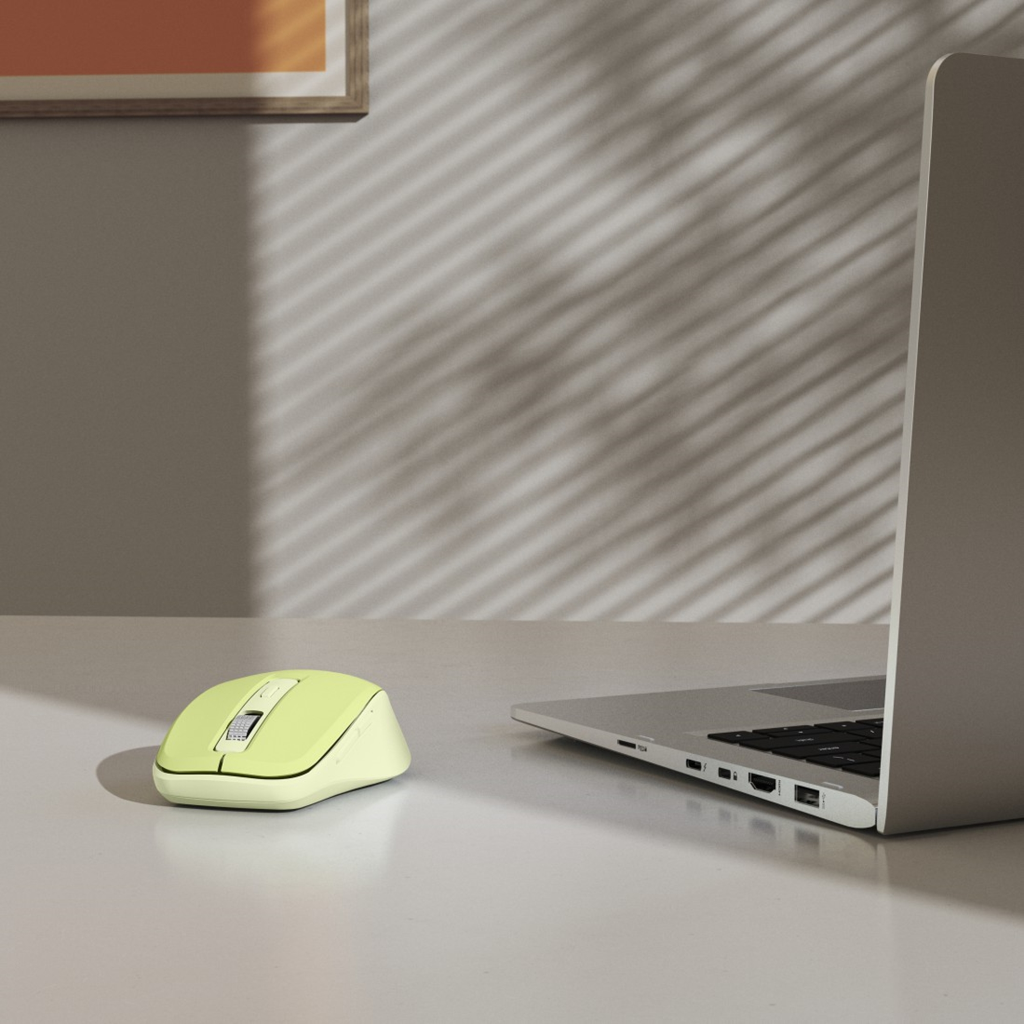 Eine gelbe Computermaus und ein Laptop stehen auf einer weißen Oberfläche. Schatten von Jalousien sind auf der Wand geworfen.