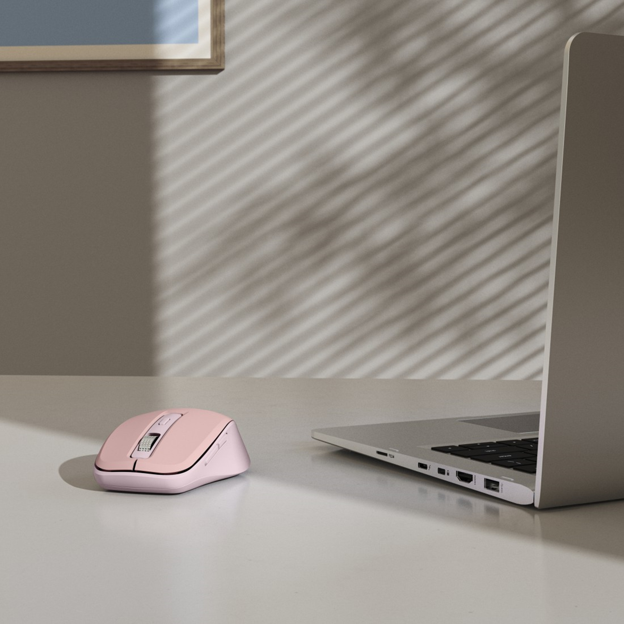 Eine rosa Computermaus liegt neben einem Laptop auf einem weißen Schreibtisch. Schatten von Jalousien an der Wand.