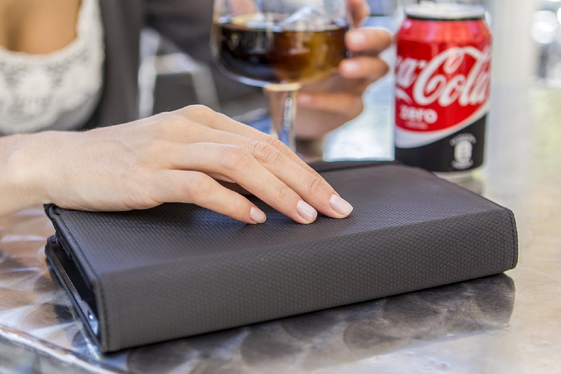 Dłoń spoczywa na czarnej, teksturowanej książce. W tle szklanka coli i puszka Coca-Cola Zero.