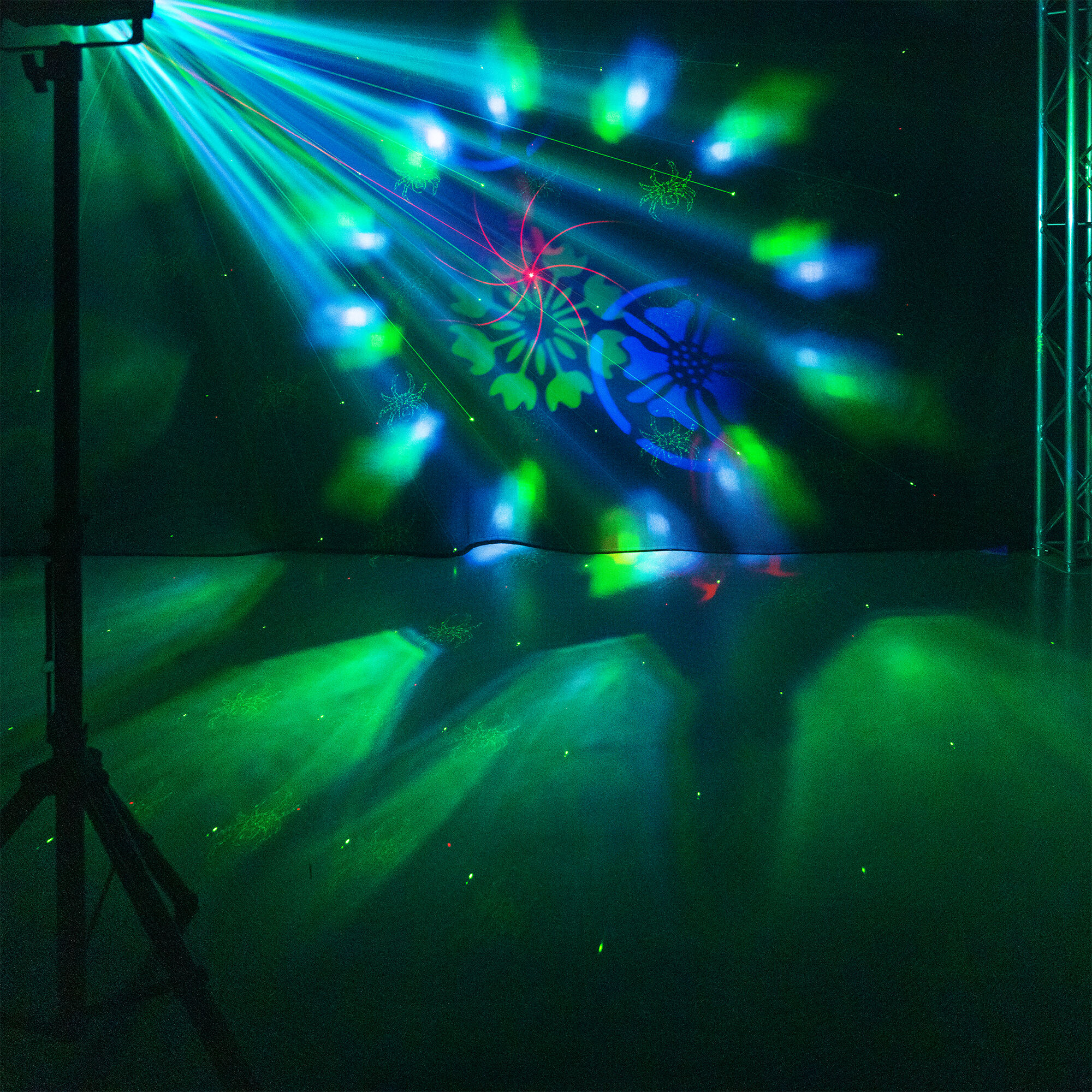 Iluminación de escenario con rayos azules y verdes. Hay un trípode en primer plano. Patrones proyectados en el fondo.