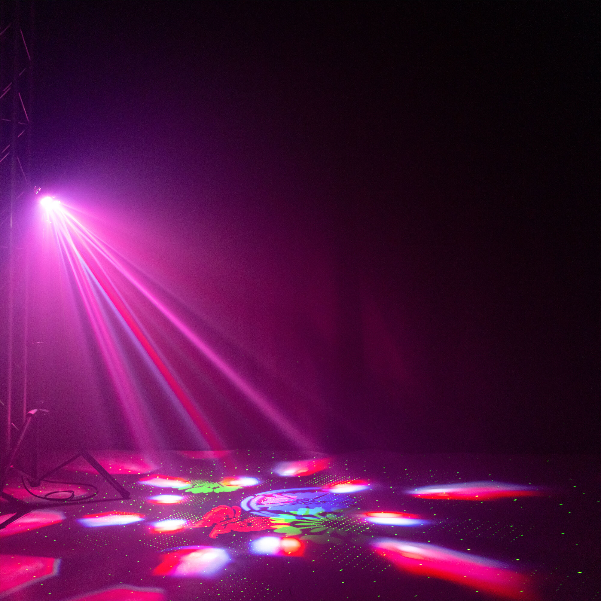 Luces brillantes rosadas de escenario brillan hacia abajo. Patrones coloridos en el suelo. Fondo oscuro.