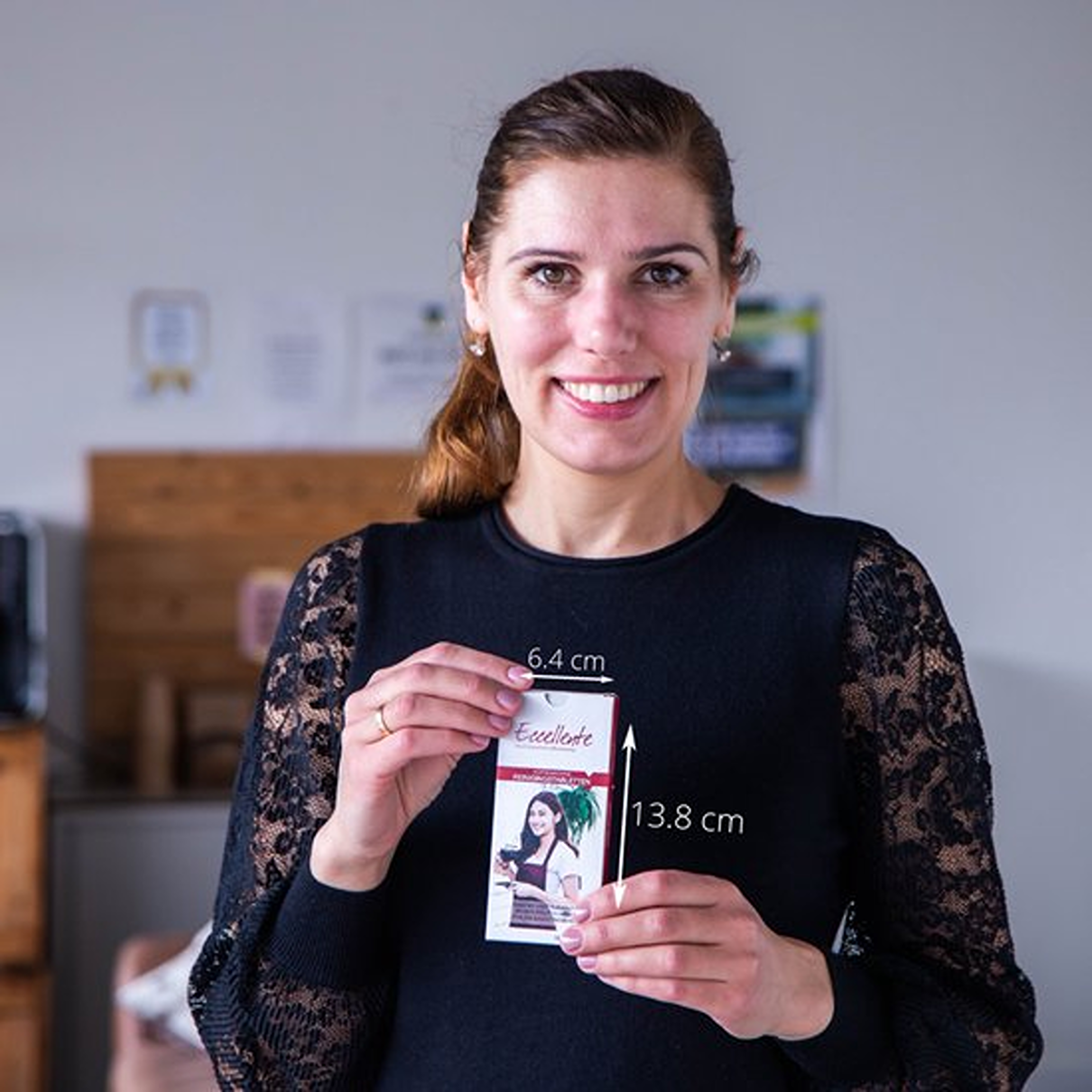 A woman smiles, holding a product box. The box is measured: 6.4cm wide, 13.8cm long. The background is a room.
