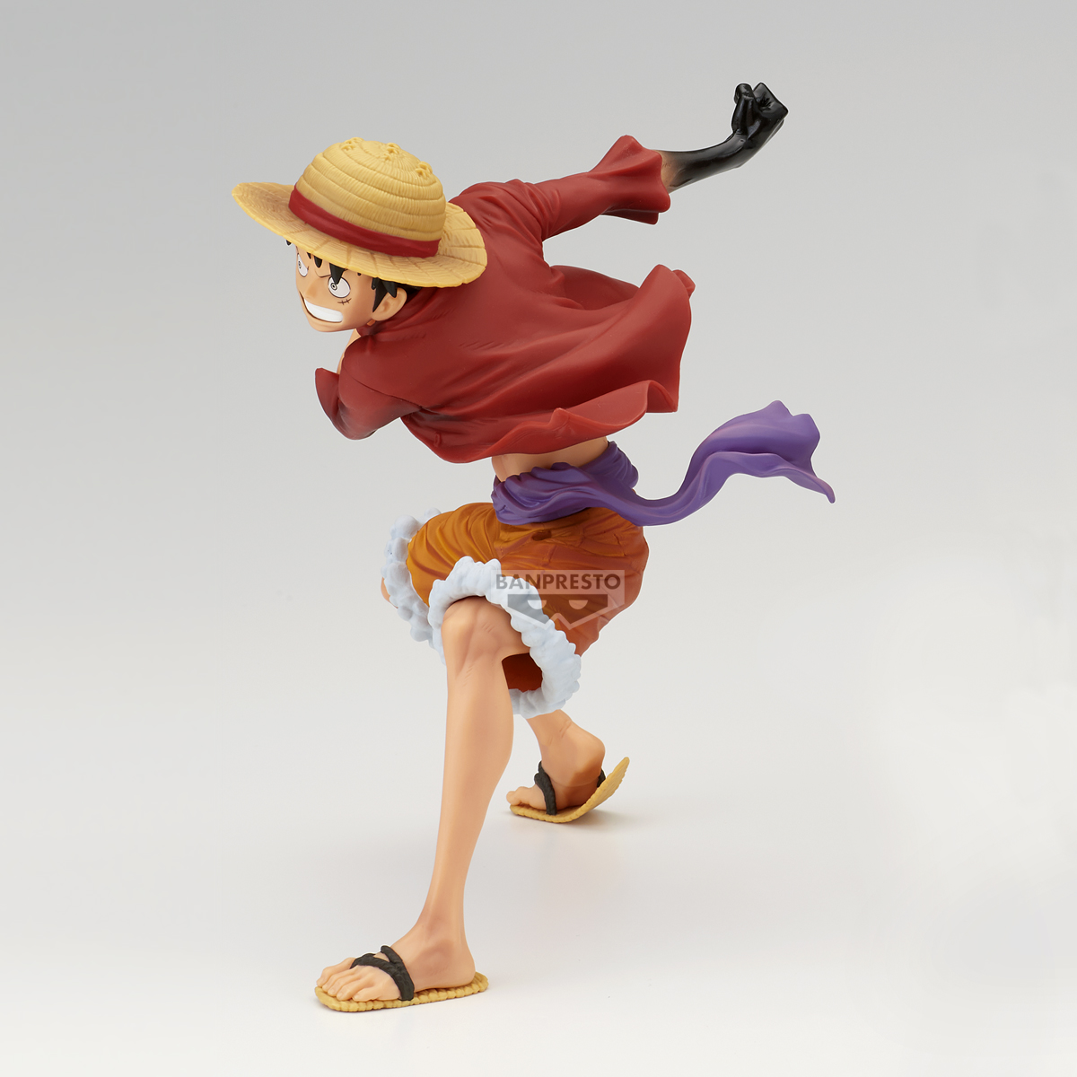 Figur einer Figur mit Strohhut, rotem Hemd, orangefarbenen Shorts und Sandalen in einer Action-Pose vor weißem Hintergrund.