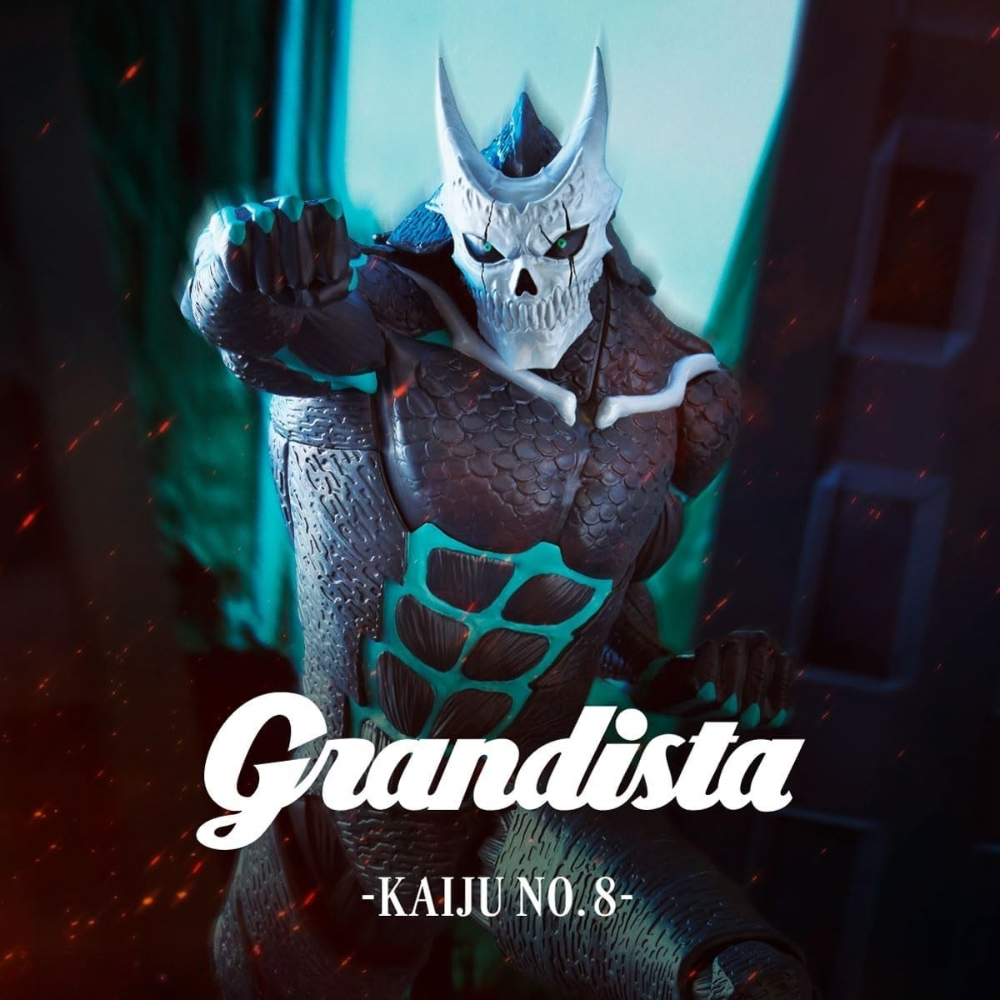 Una figura di kaiju con testa a forma di teschio e corna, armatura scura e dettagli turchesi. La parola "Grandista" è scritta sull'immagine.