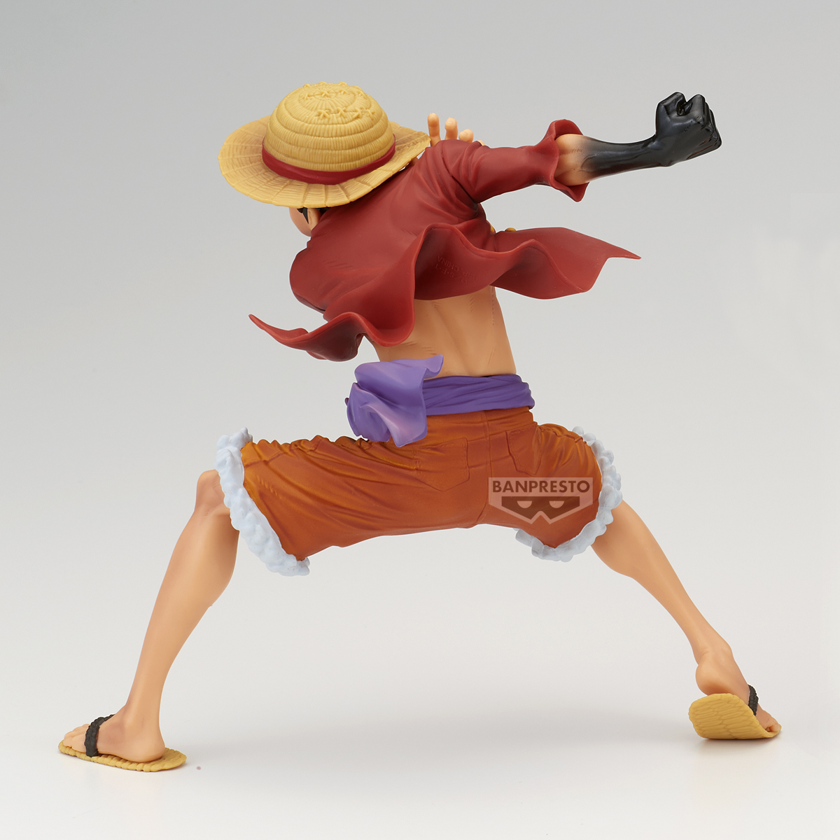 Figur einer Figur in Aktion. Er trägt einen Strohhut, ein rotes Hemd, orange Shorts und Sandalen. Sein Arm ist schwarz, die Faust geballt.