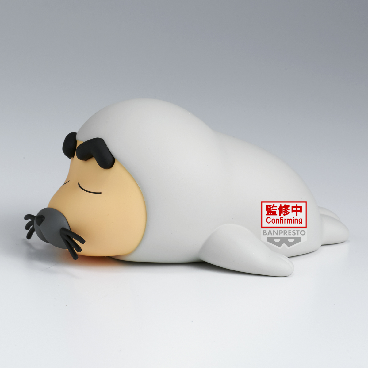Una statuetta di foca grigia giace su una superficie bianca. Ha un viso beige, occhi neri e baffi. È visibile un adesivo rosso 'Confirming'.