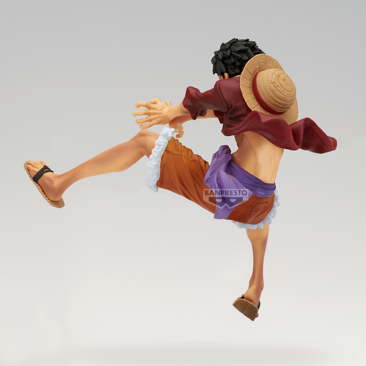 Statuetta di un uomo in azione. Indossa una camicia rossa, pantaloncini arancioni e un cappello di paglia. Sta calciando. Sfondo bianco.