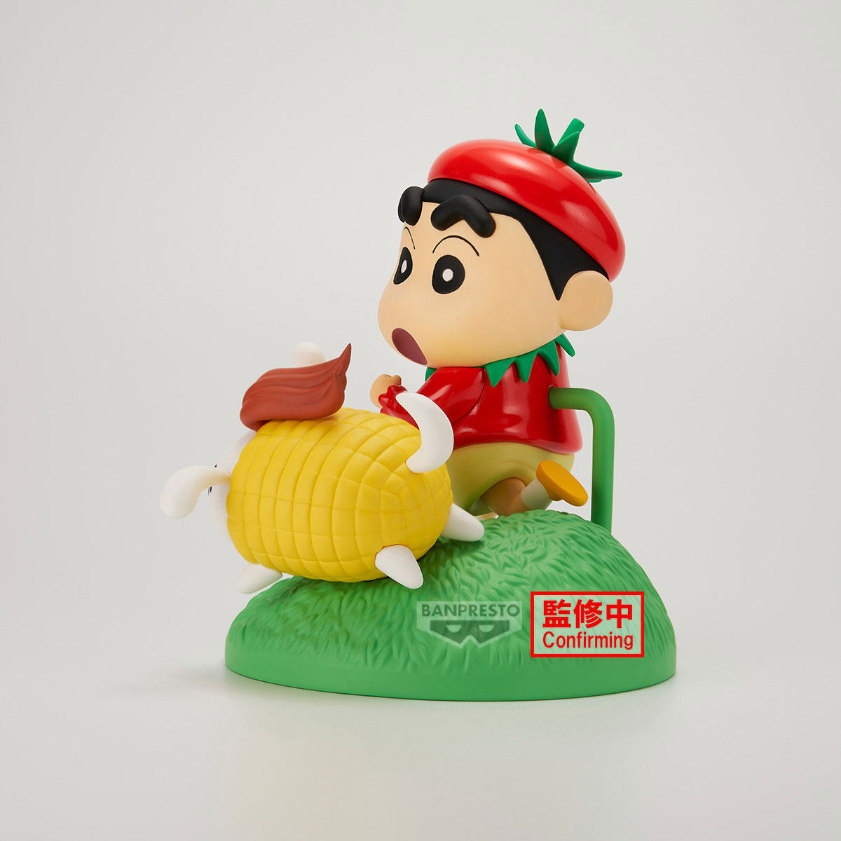 Una figura di Shin-chan con cappello e camicia rossi. Cavalca una creatura a forma di mais su una base verde. Testo 'Confirming'.